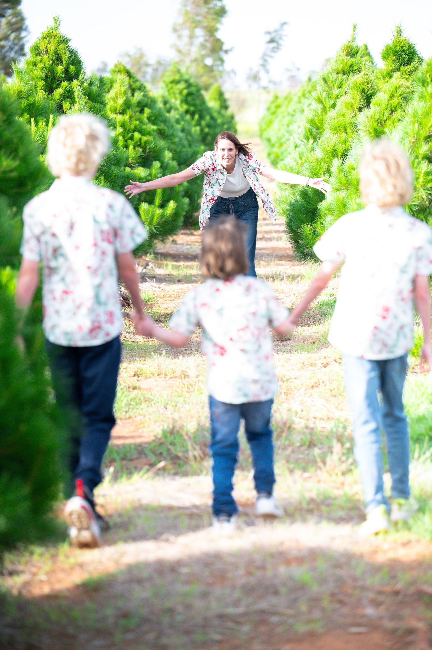 Playful family walking through rows of evergreen trees wearing matching outfits.