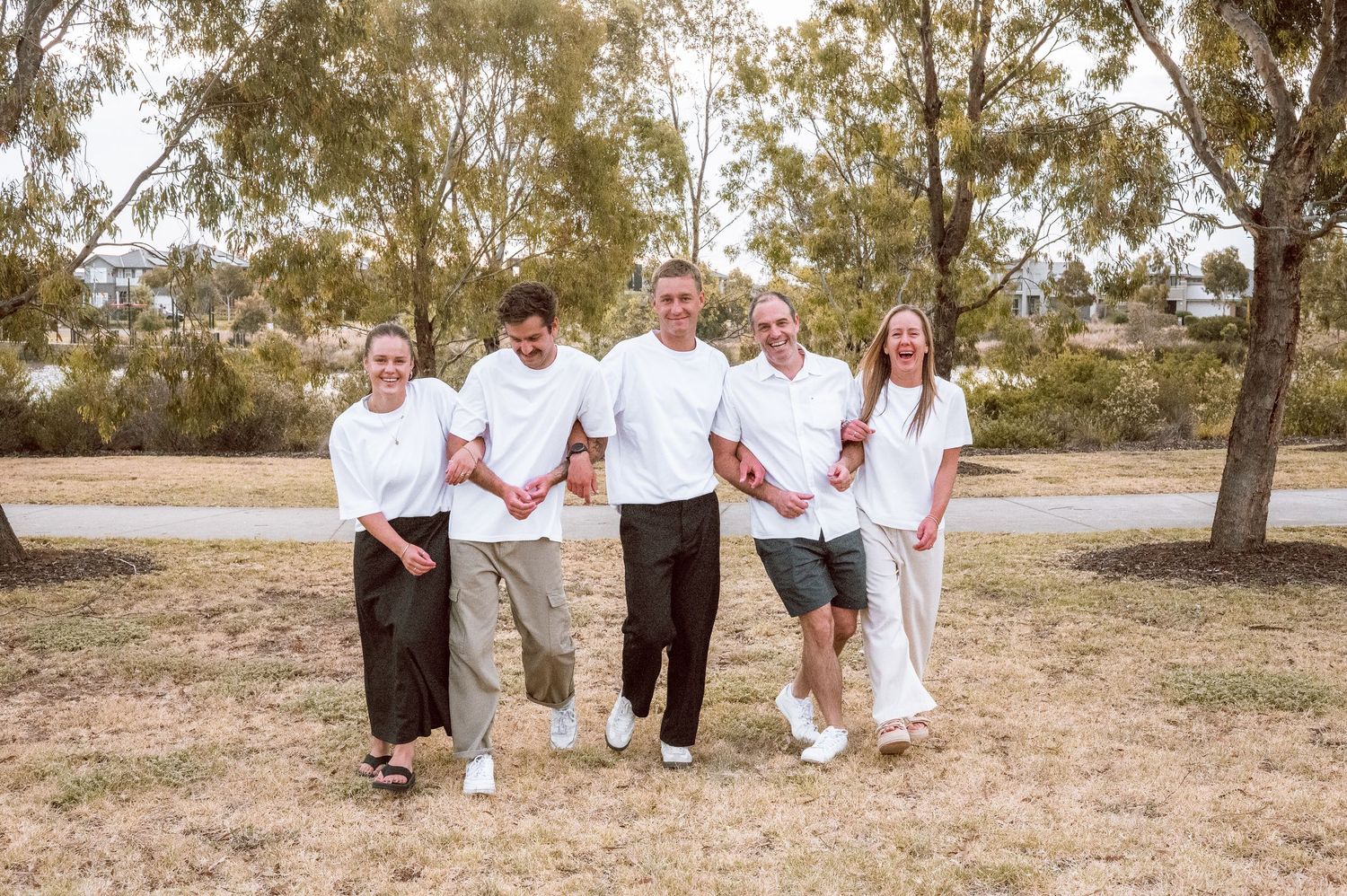 A group in white tops poses together on a path with eucalyptus trees in the background.