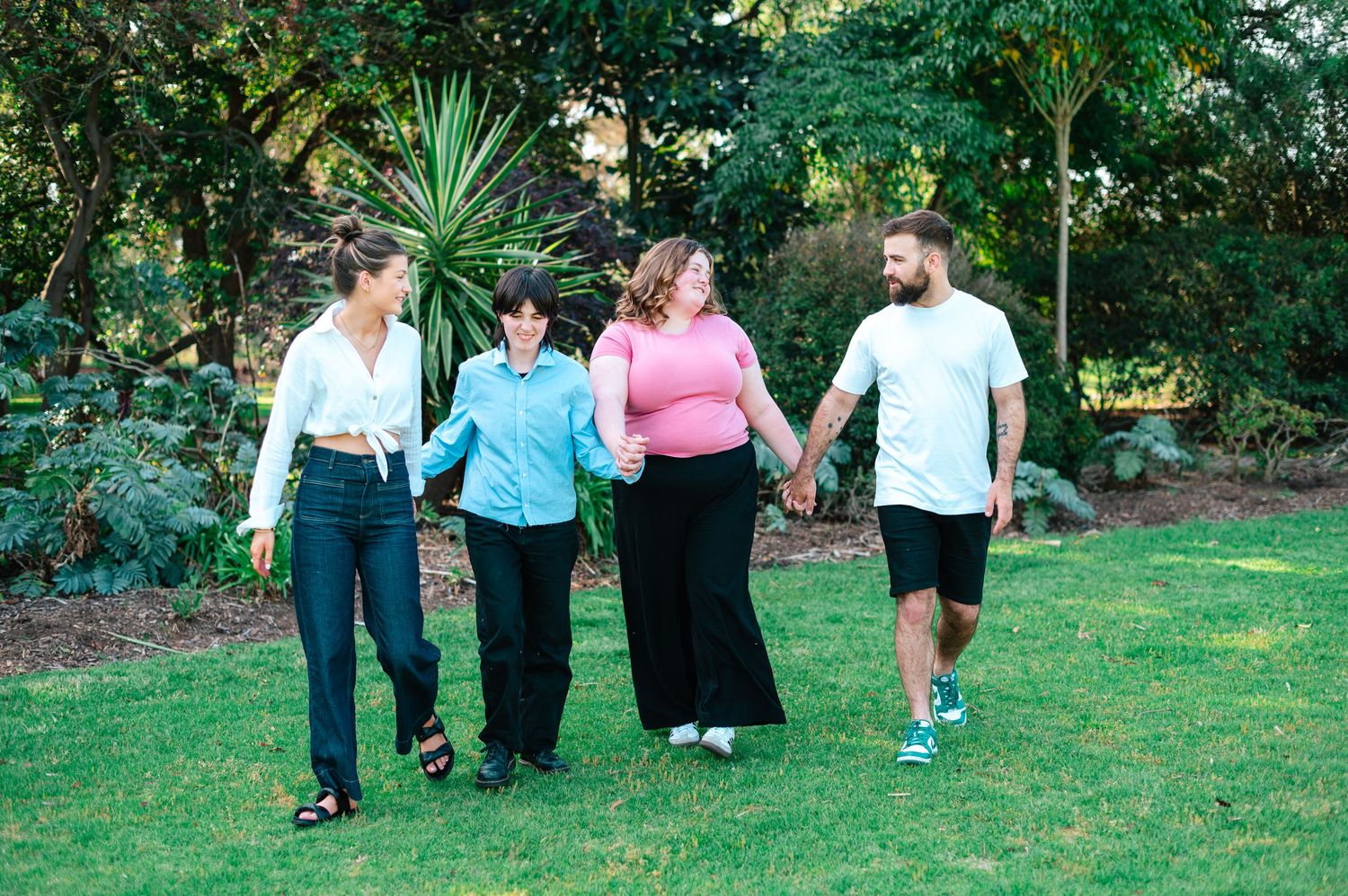 Friends arranged in a line outdoors with greenery and architectural elements in background.
