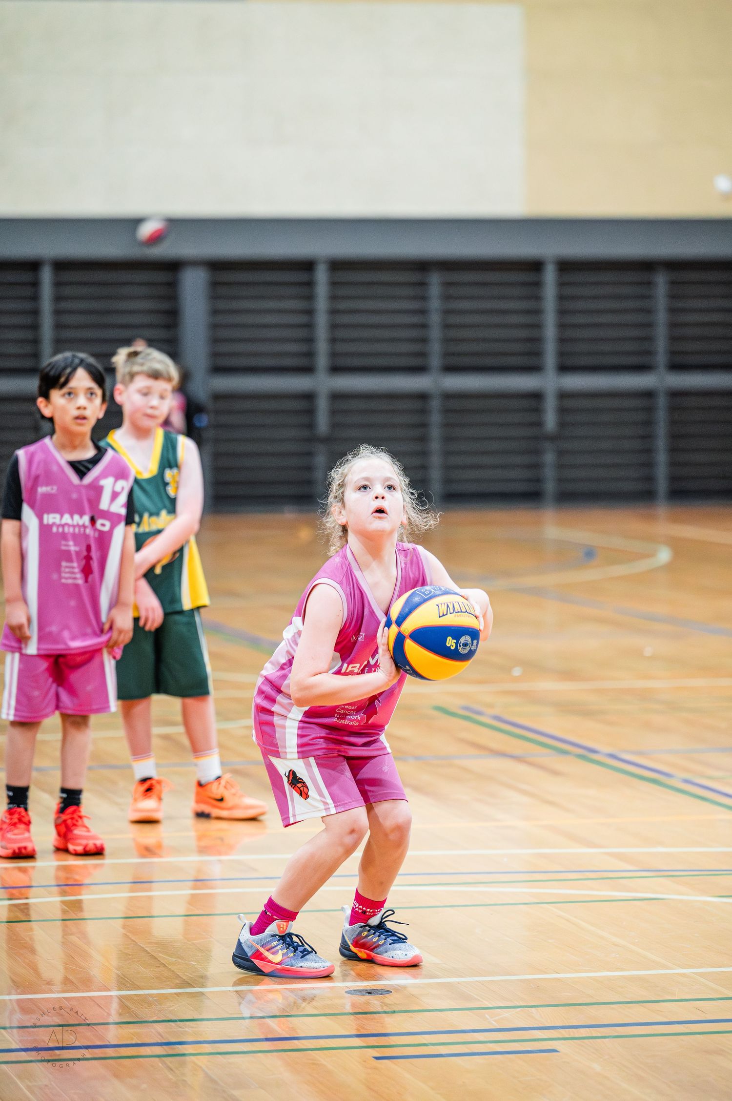 Young girl in pink uniform prepares to shoot a basketball during a junior indoor basketball game.