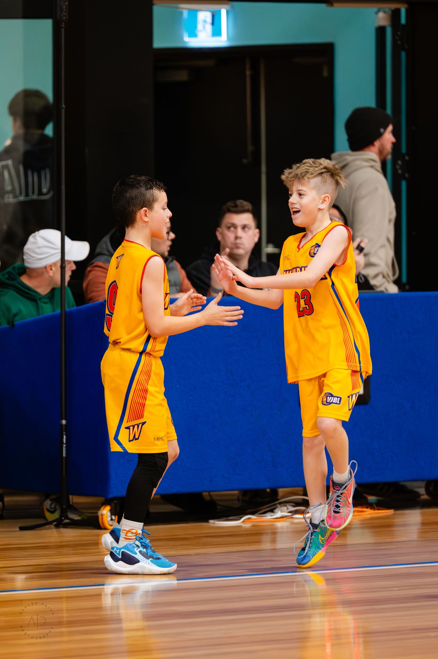 Two young boys in yellow basketball uniforms high-fiving on an indoor court during a youth basketball game.
