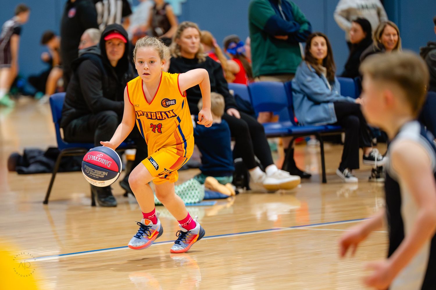Young girl in yellow jersey dribbling basketball during indoor youth league game.