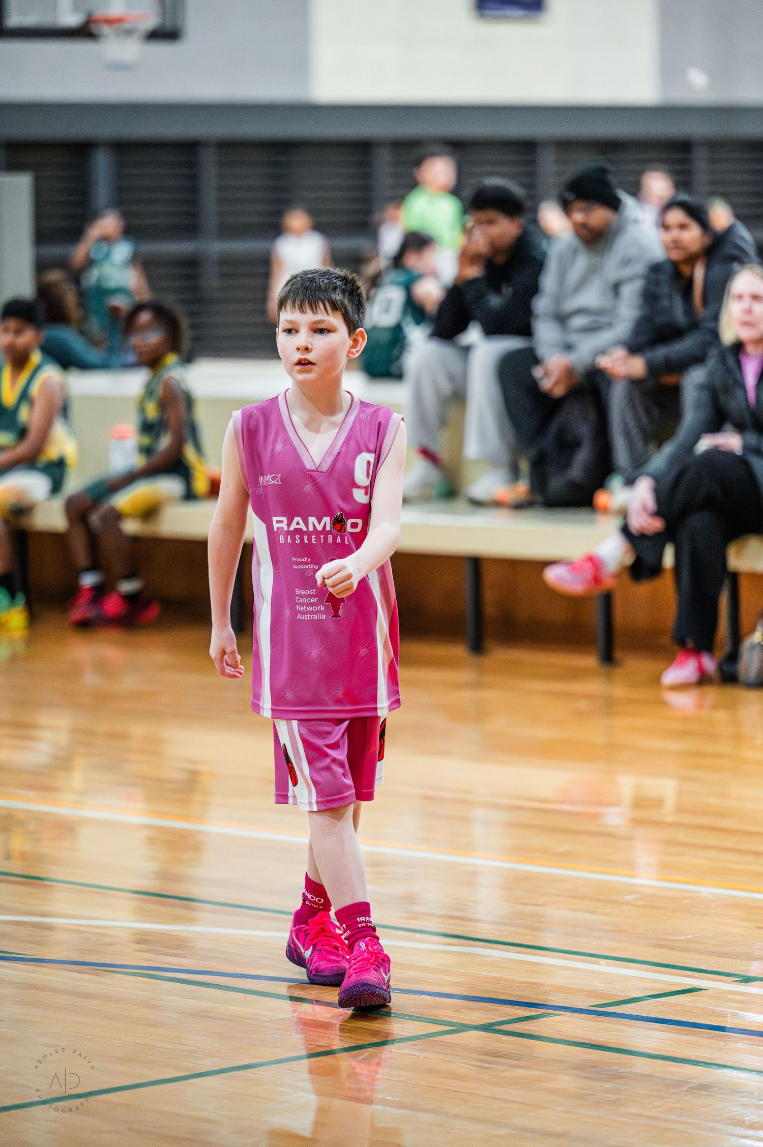 Young boy in pink RAMBO Basketball uniform dribbling on indoor court during youth basketball game.