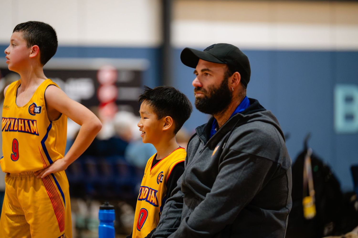 Youth basketball players in yellow uniforms stand beside a coach during a game on an indoor court.