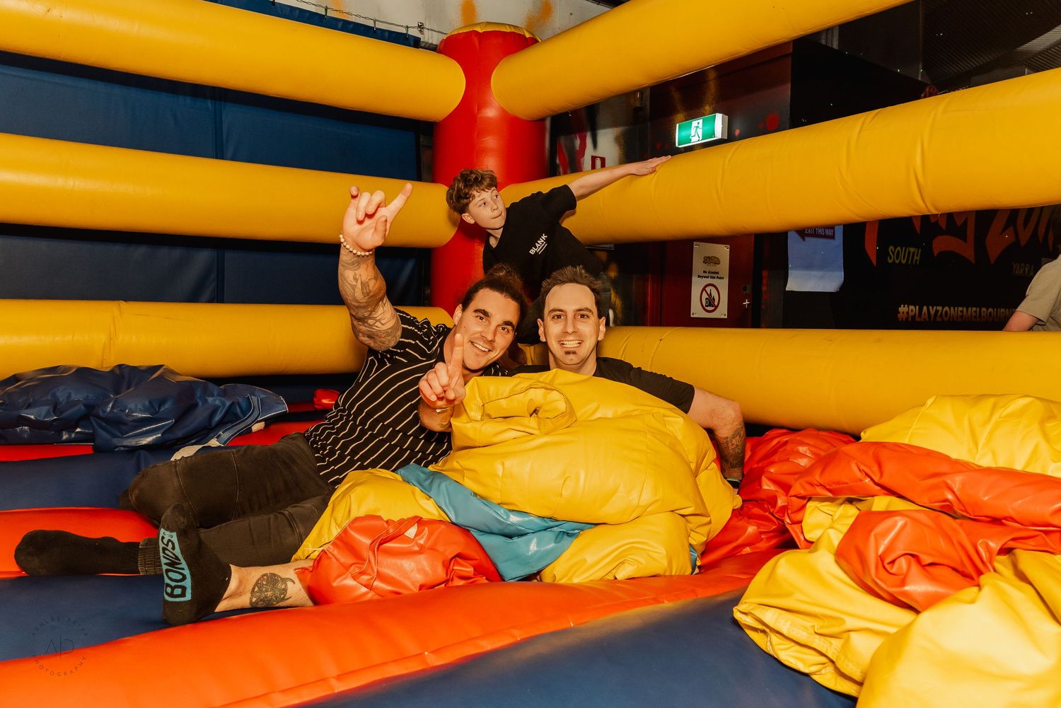 Two friends smiling and posing inside a colorful yellow and orange bouncy castle inflatable.