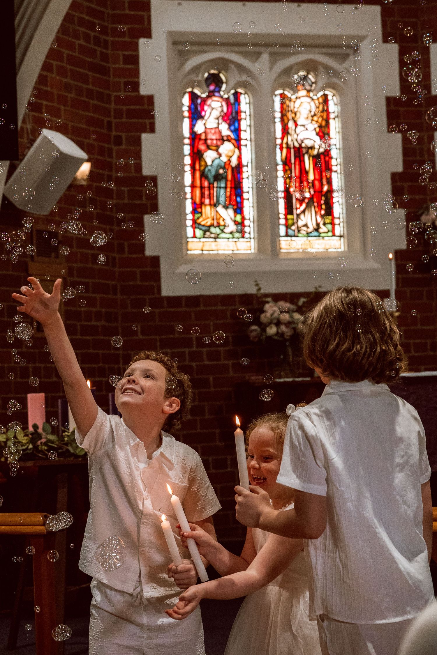 Children play with bubbles beneath stained glass windows in a church.