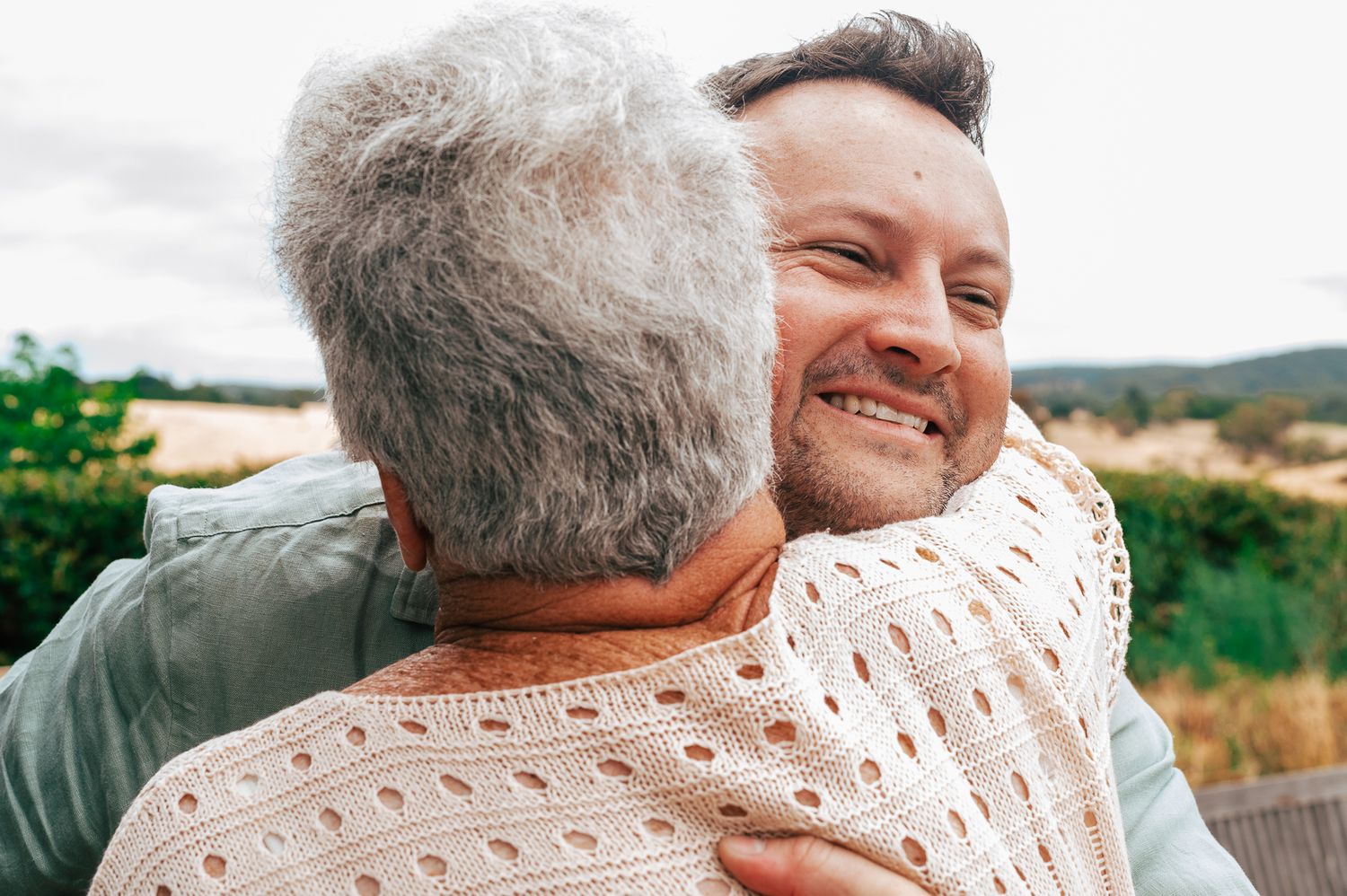 Two people share a warm embrace outdoors while smiling and showing genuine affection.