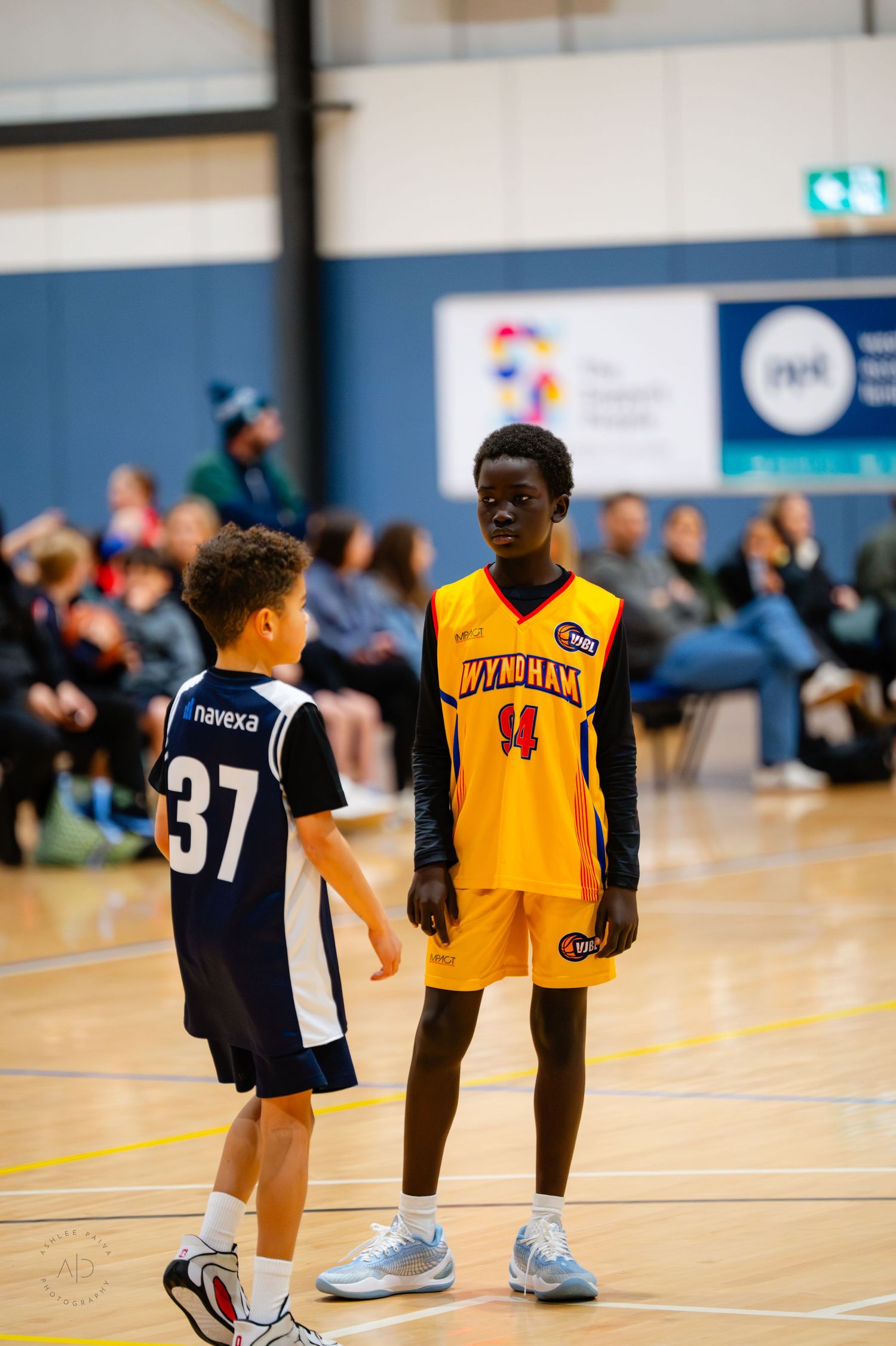 Two youth basketball players in jerseys numbered 37 and 44 stand on an indoor court during a game.