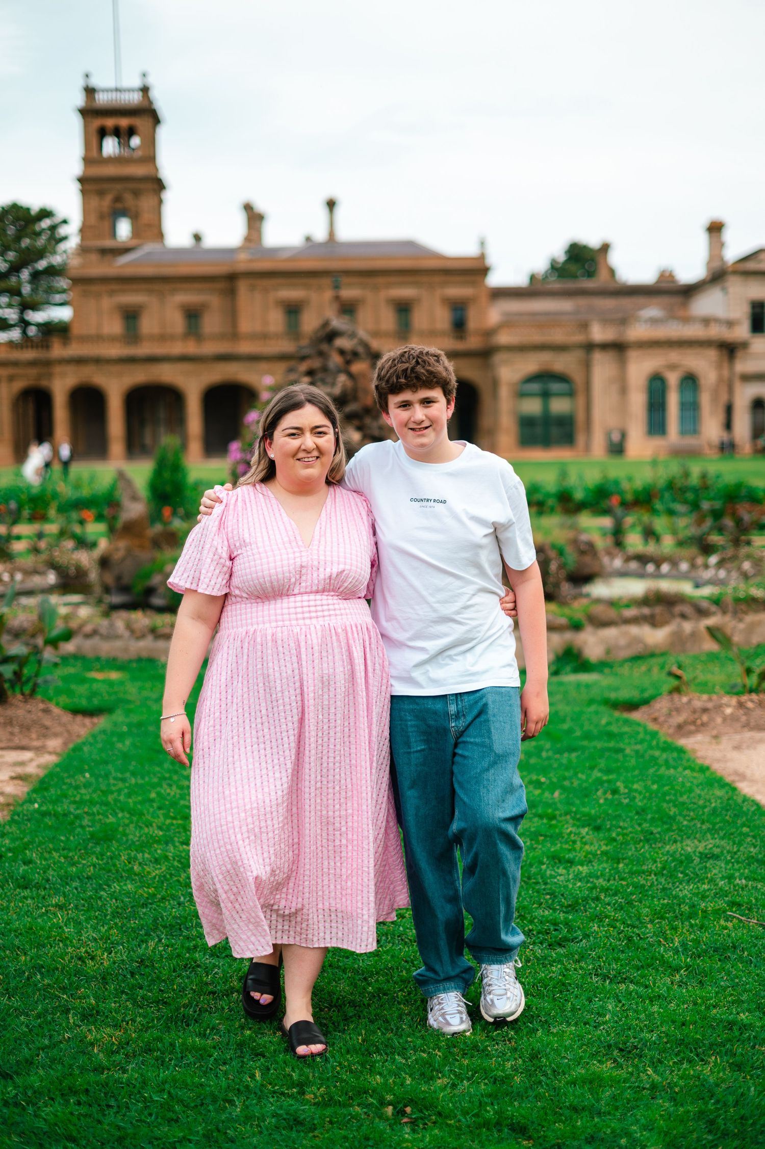 Two people walking on grass with a beautiful historic building and tower in the background.