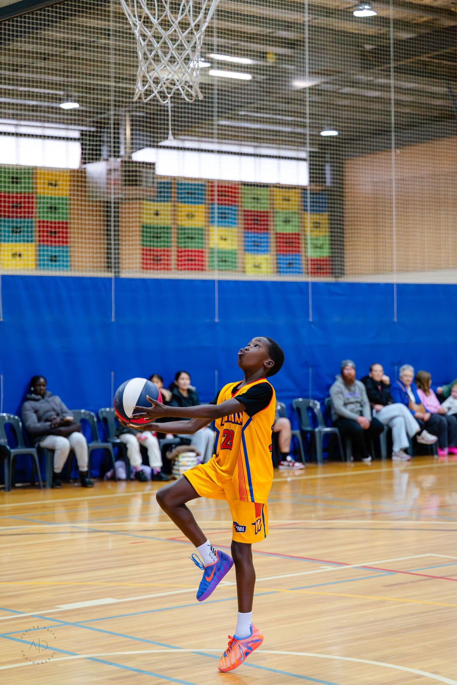 Young basketball player in yellow uniform leaping to shoot in an indoor gymnasium during a youth basketball game.