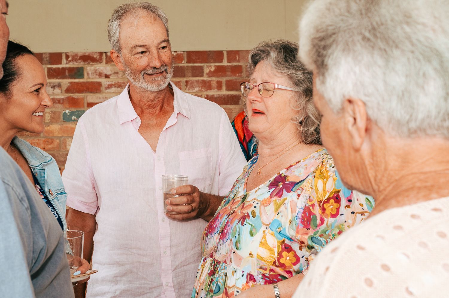 A group of seniors socialize together at a gathering with a brick wall backdrop.