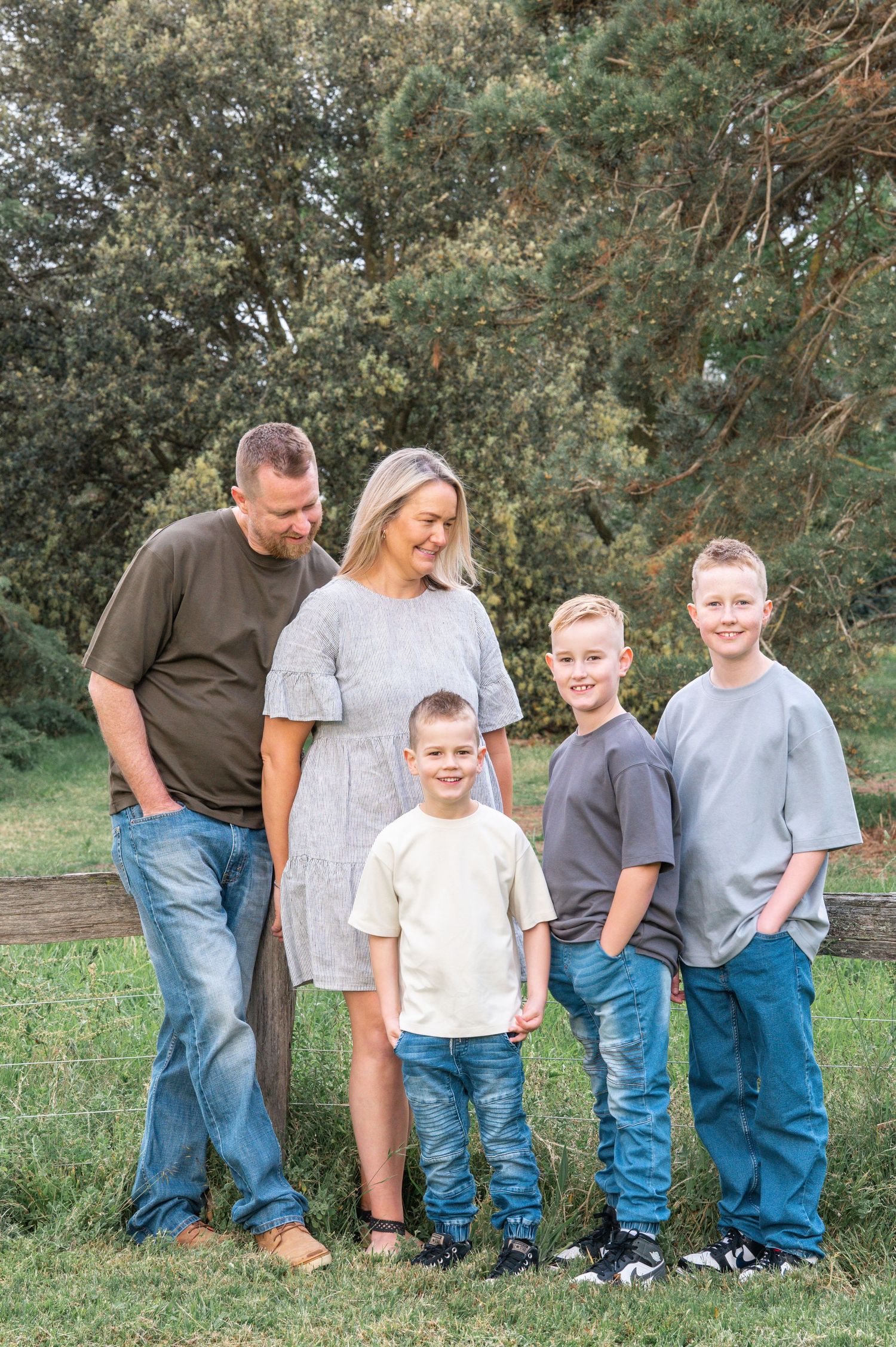 Full family portrait in casual attire against lush green outdoor background.