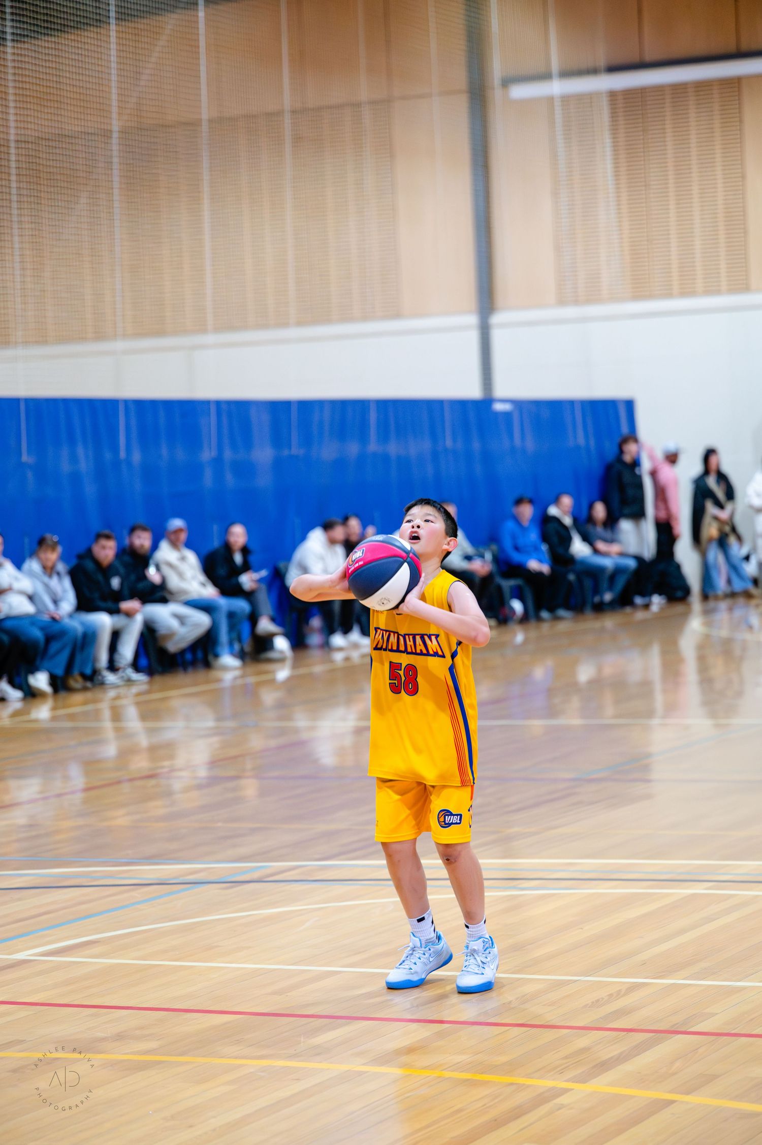 Young basketball player in yellow uniform #58 shooting the ball during an indoor game with spectators watching.