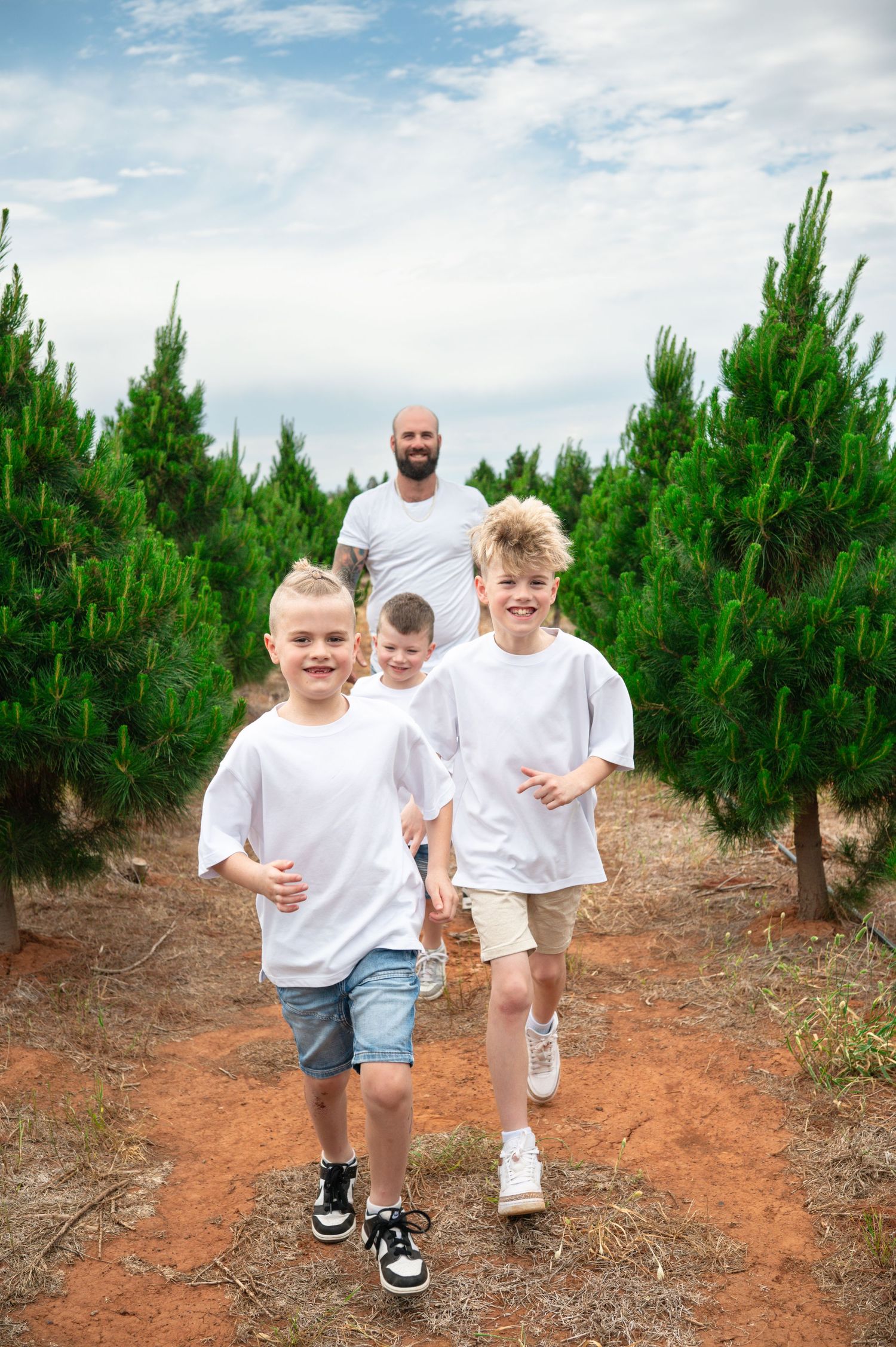 Group walking along a red dirt path between rows of pine trees.