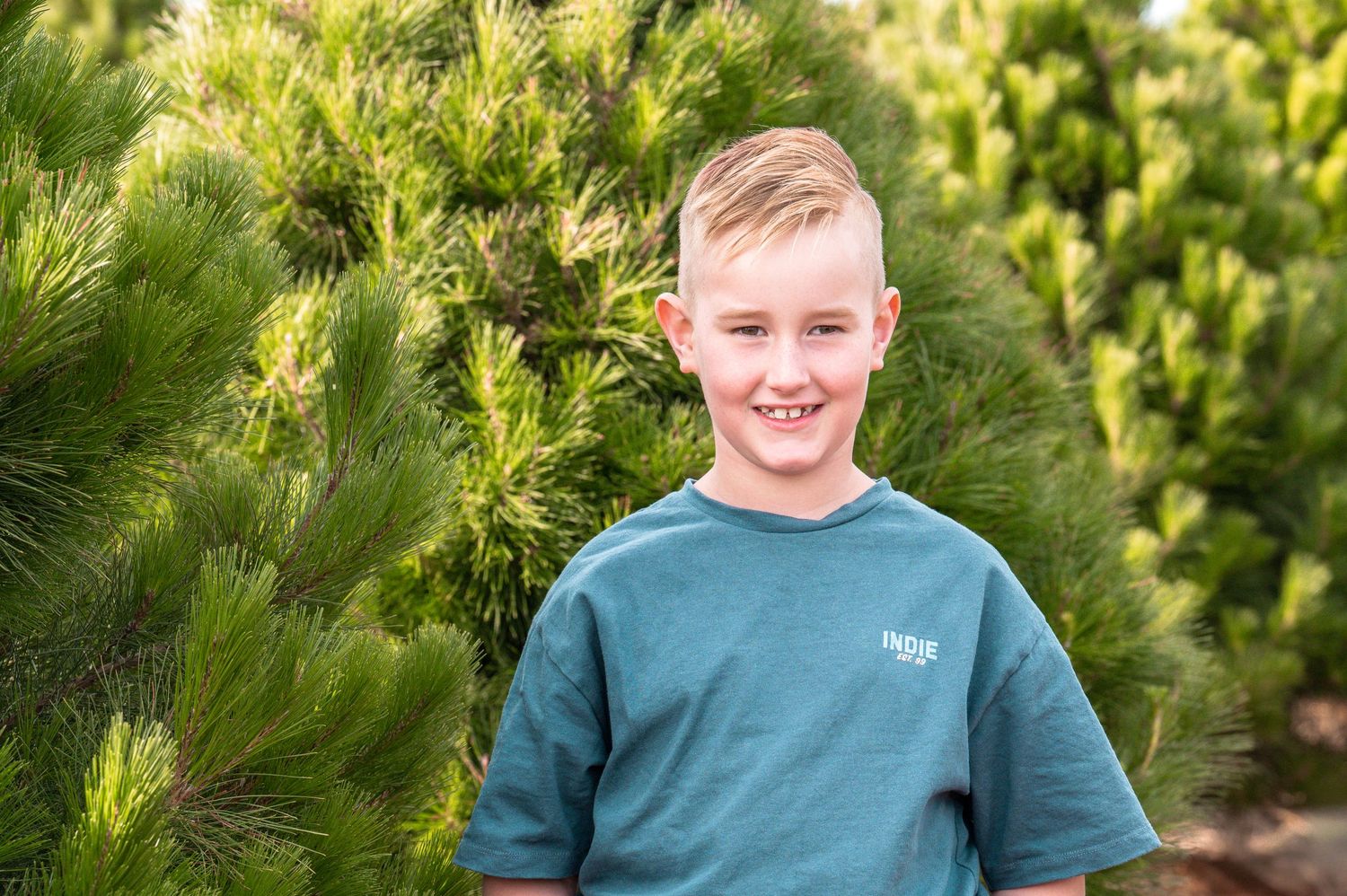 Smiling portrait taken outdoors with lush evergreen trees in background.