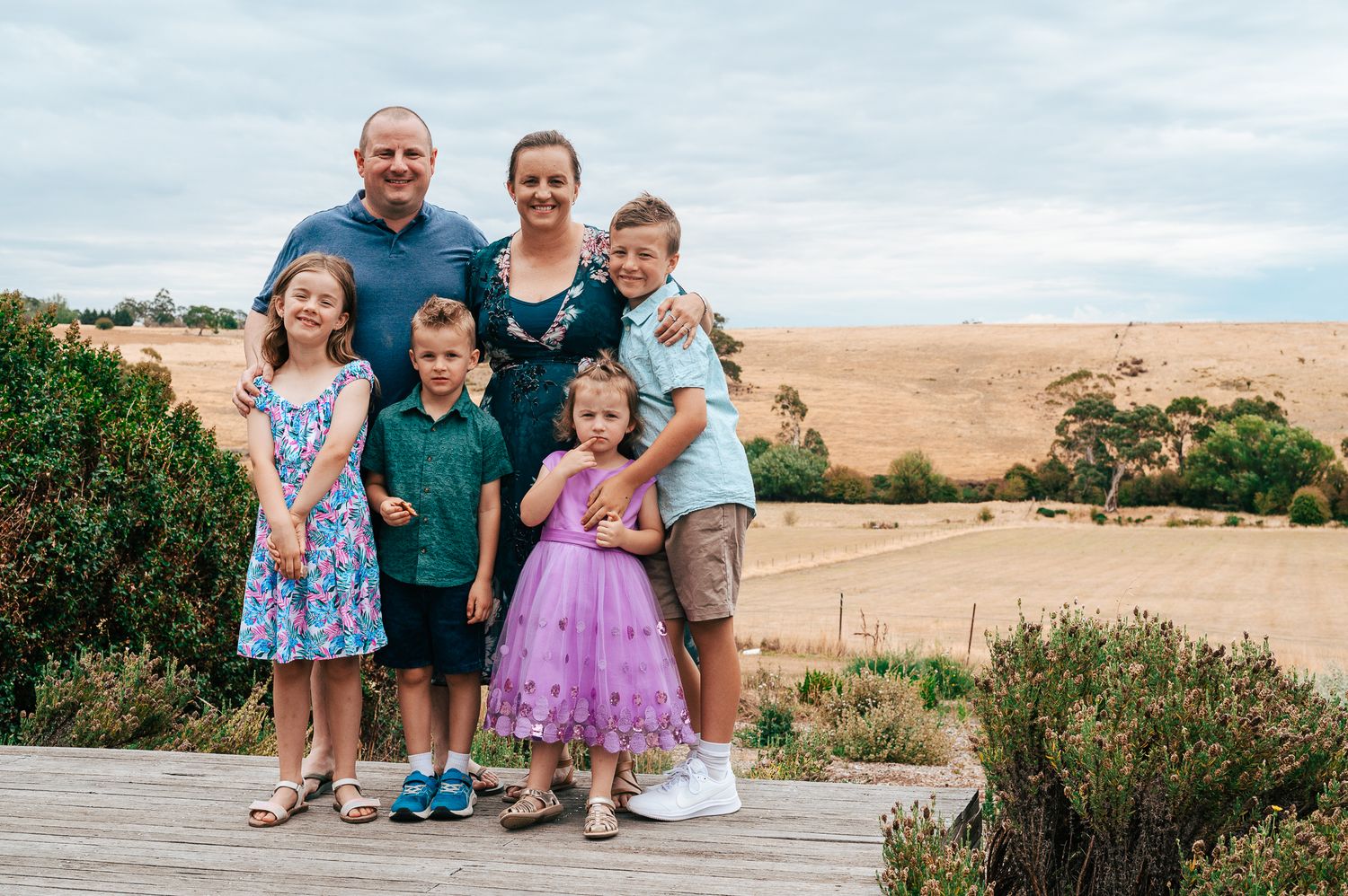 A group stands together on a wooden boardwalk overlooking rolling hills and dry grasslands on a cloudy day.