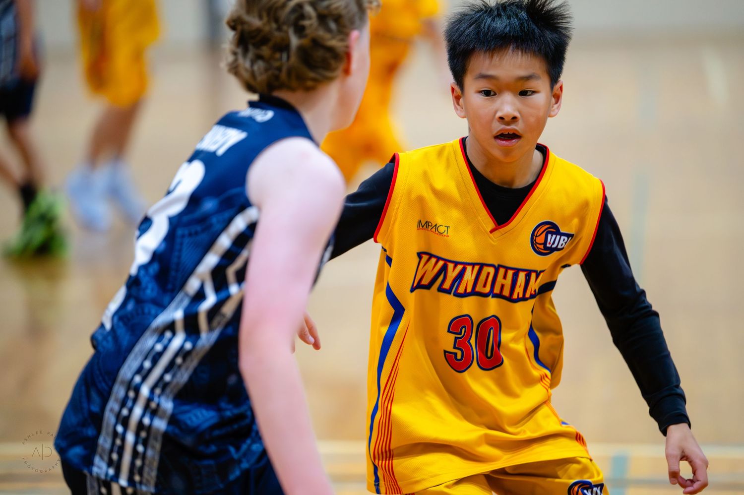 Young basketball player in Wyndham #30 yellow jersey dribbles past defender in indoor youth basketball game.