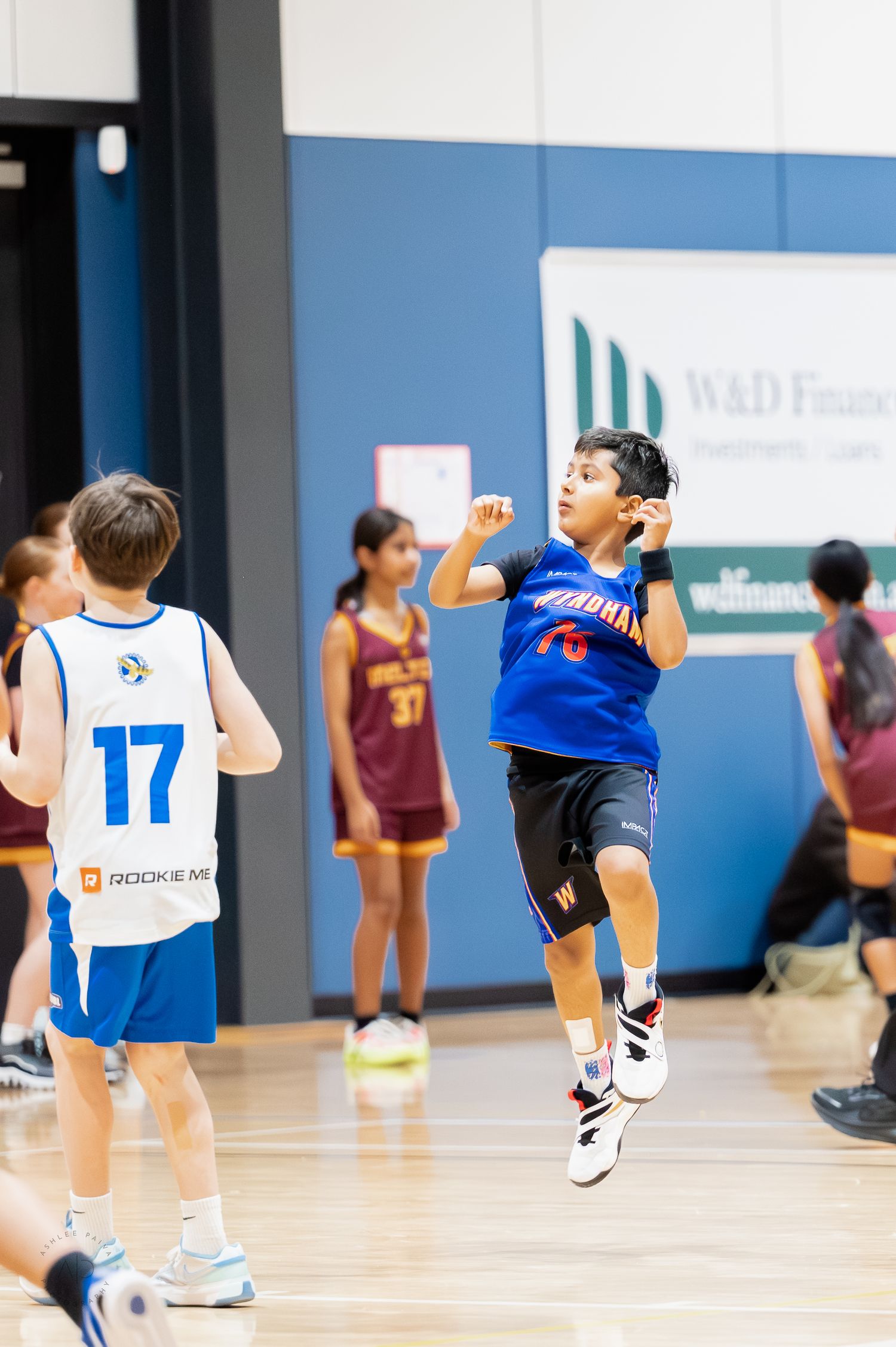 Young boy in blue jersey jumps to pass during a youth basketball game in an indoor gymnasium.