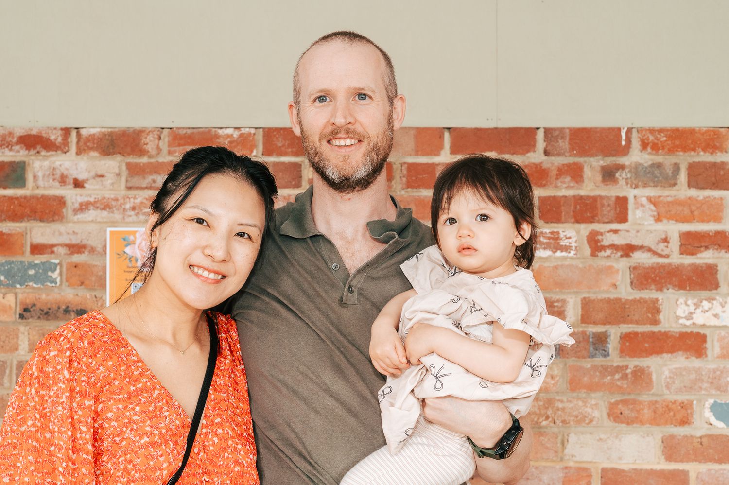 A family poses together in front of a rustic brick wall for a casual portrait session.