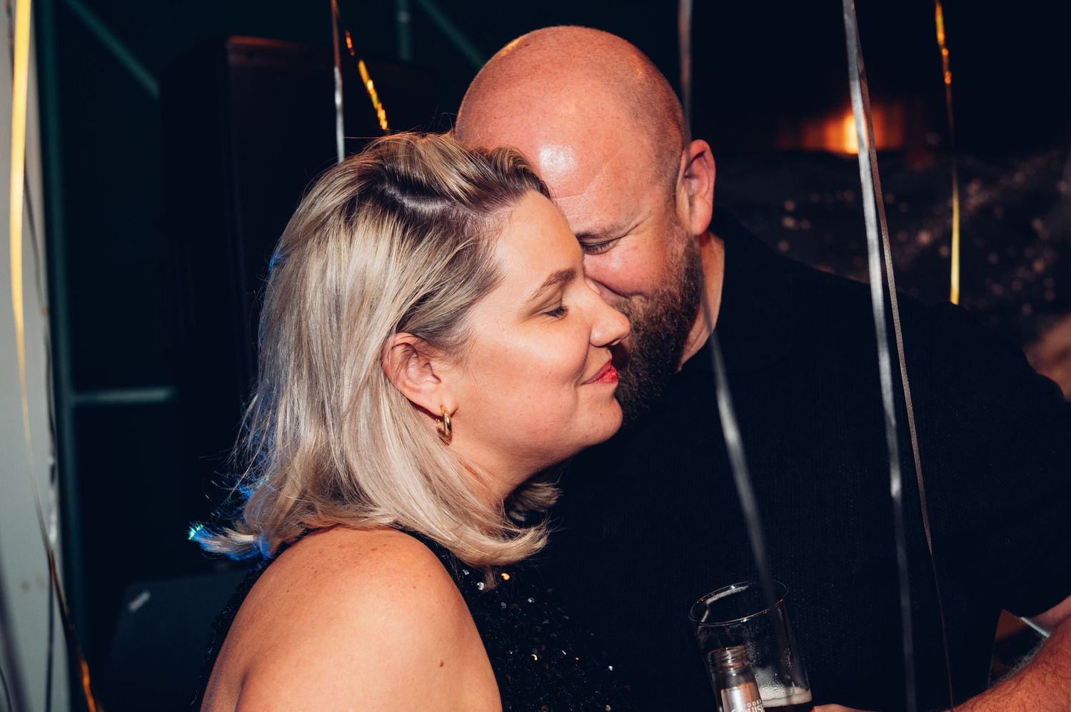 Couple sharing an intimate moment at a dimly lit party venue.