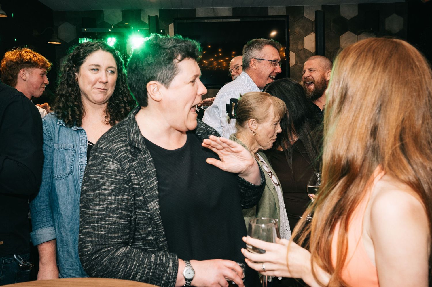 Party guests mingling and chatting at a social gathering with green lighting.