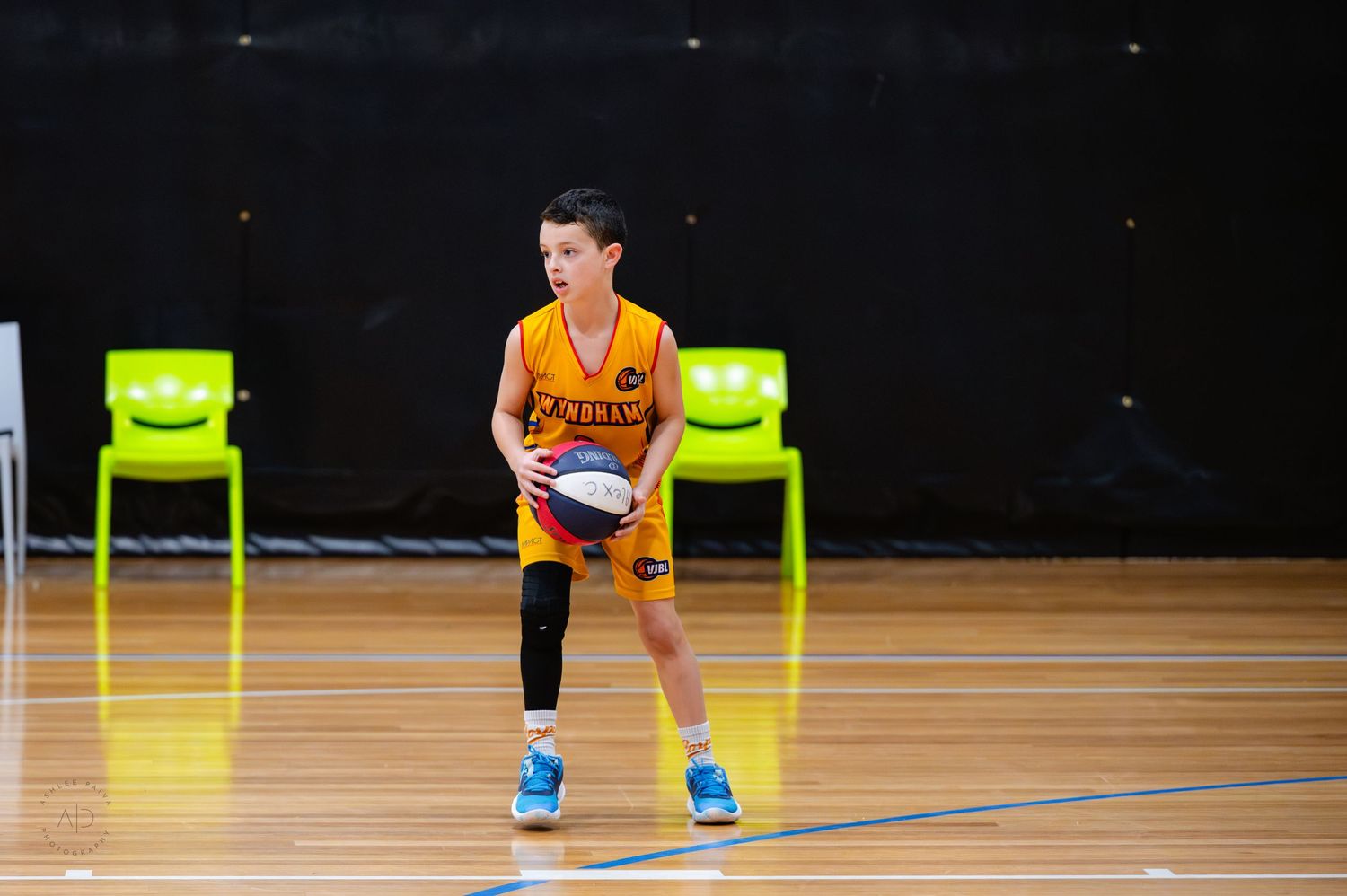 Young boy in orange basketball uniform dribbling ball on indoor court during youth basketball game.