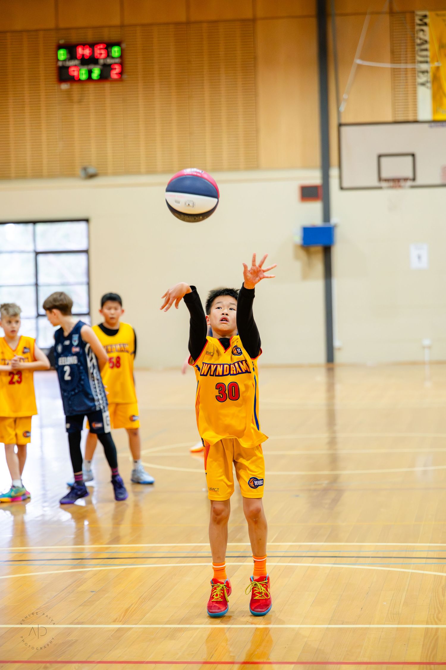 Young boy in yellow jersey #30 shooting basketball during indoor youth league game.