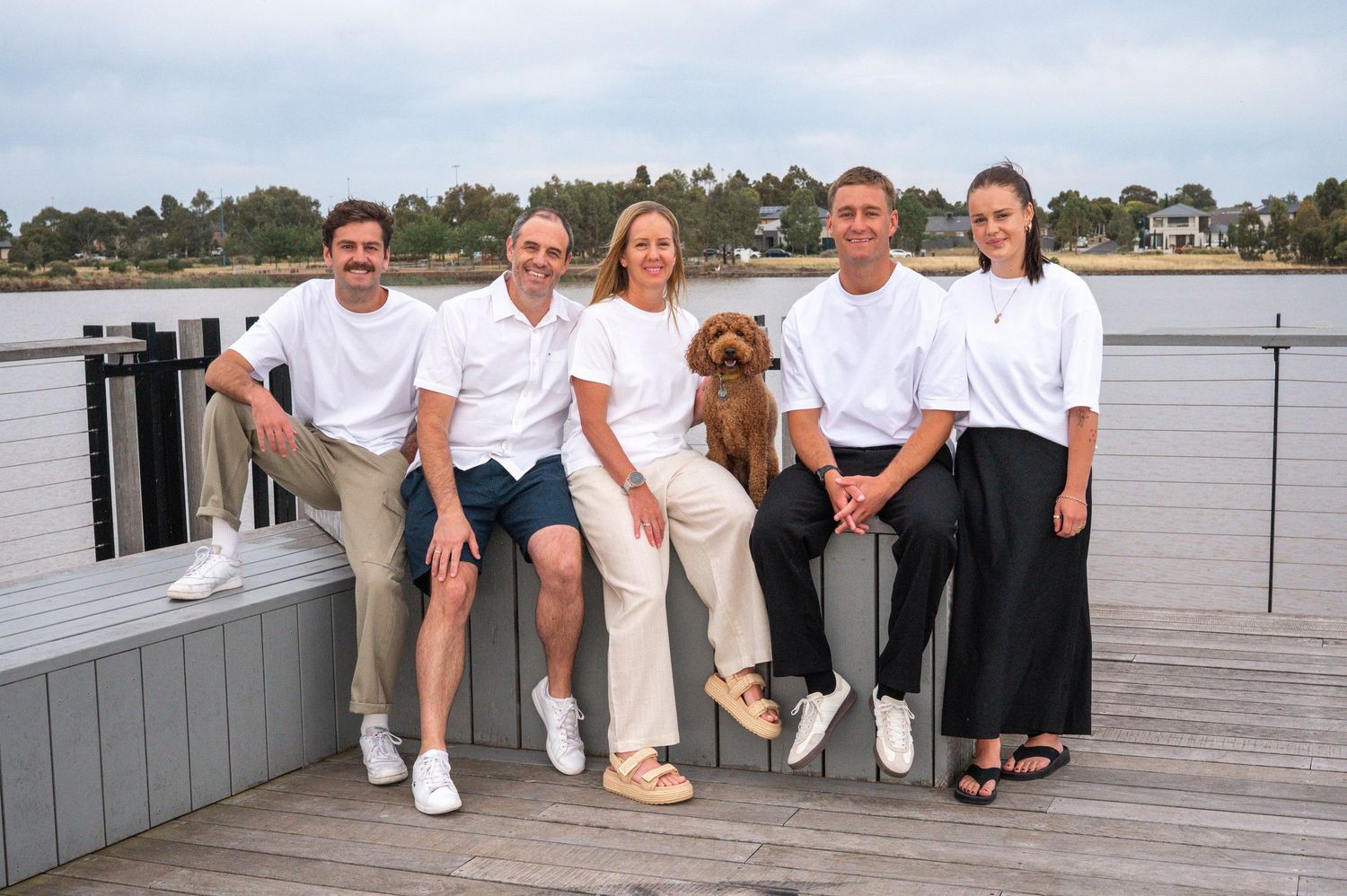 A group in white shirts poses on a deck with a brown dog sitting among them.