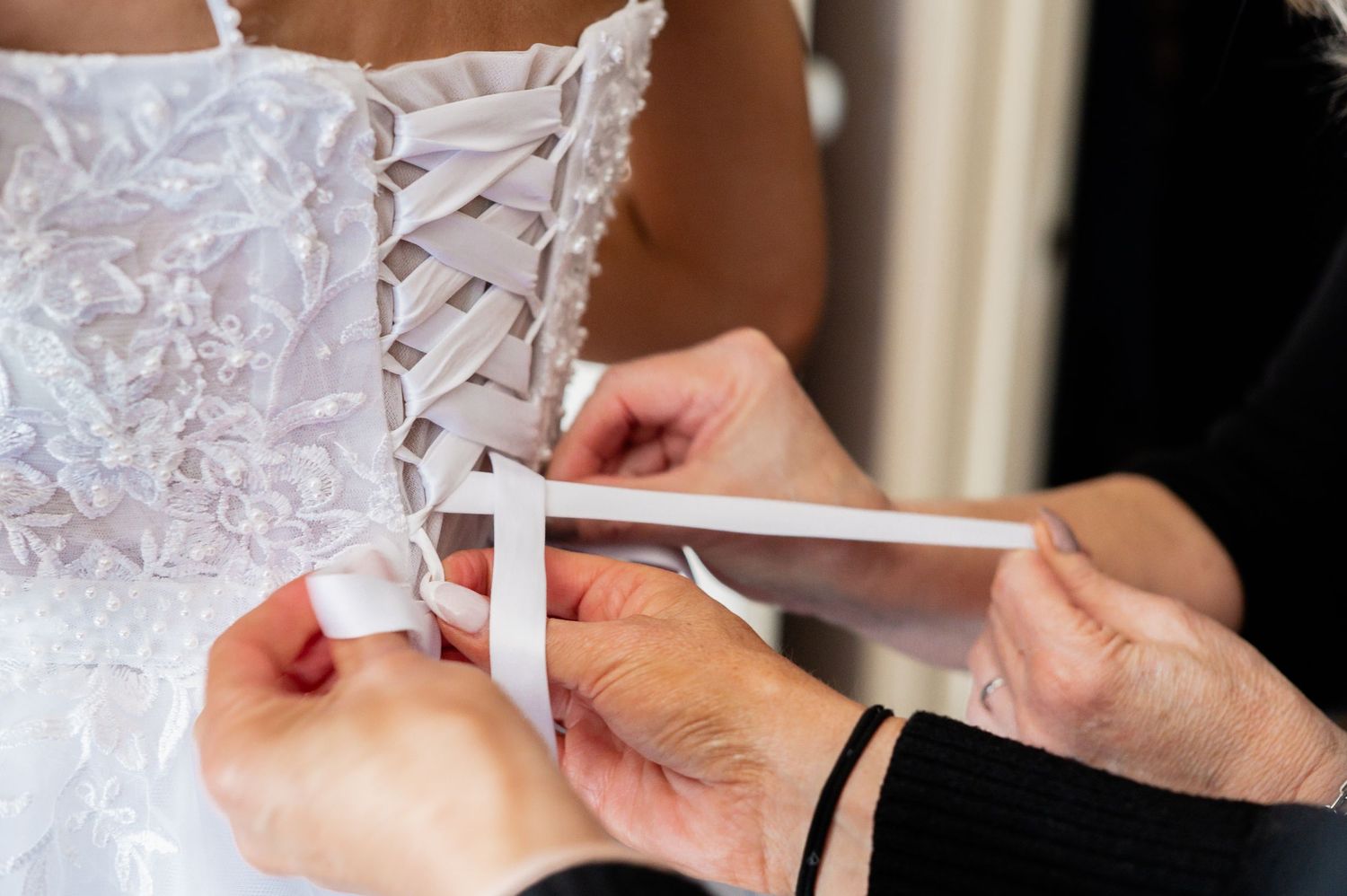 Hands lacing up a white bridal corset wedding dress with ribbon on the back of a bride.