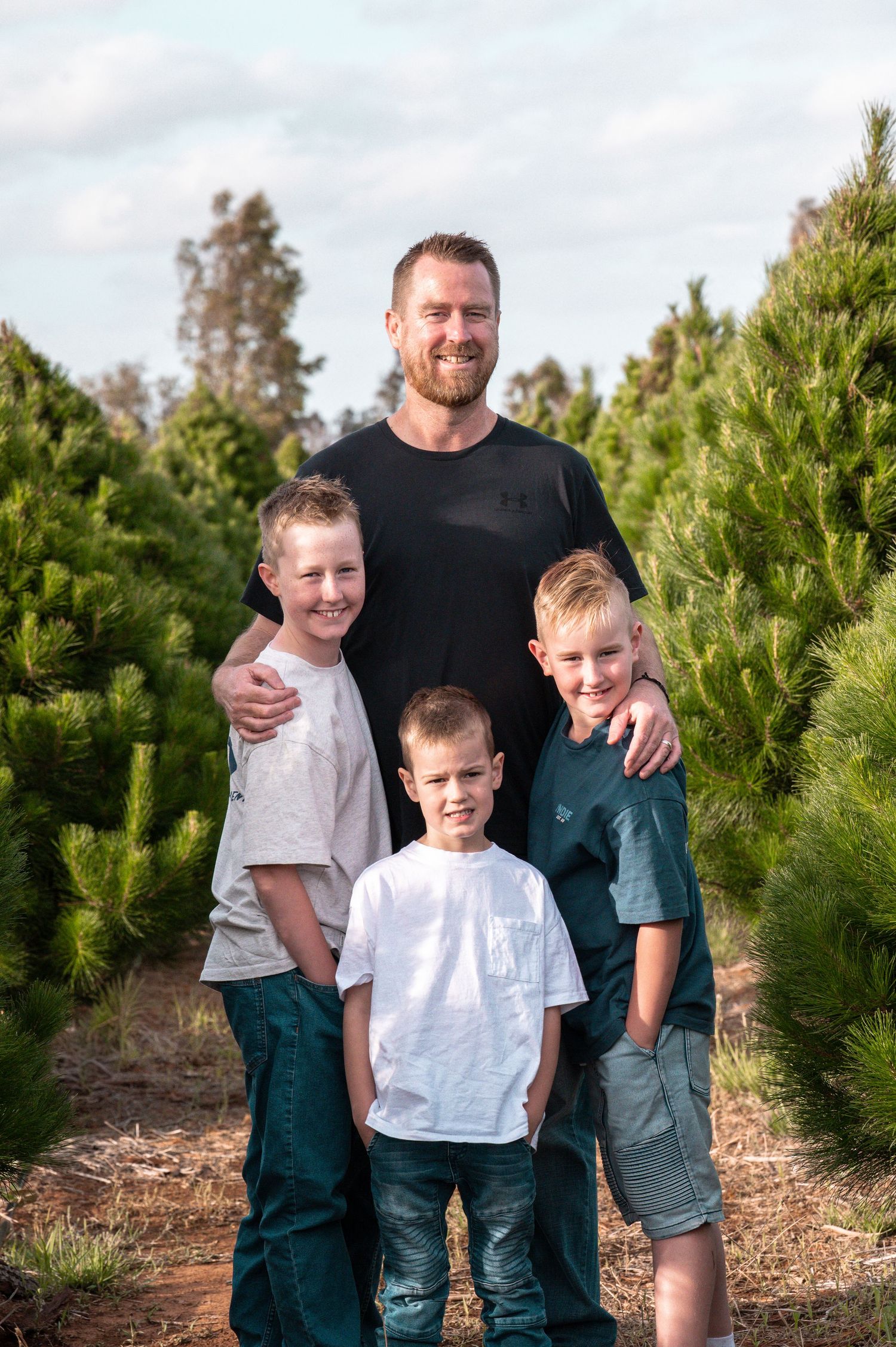 Casual outdoor family photo session between rows of pine trees.