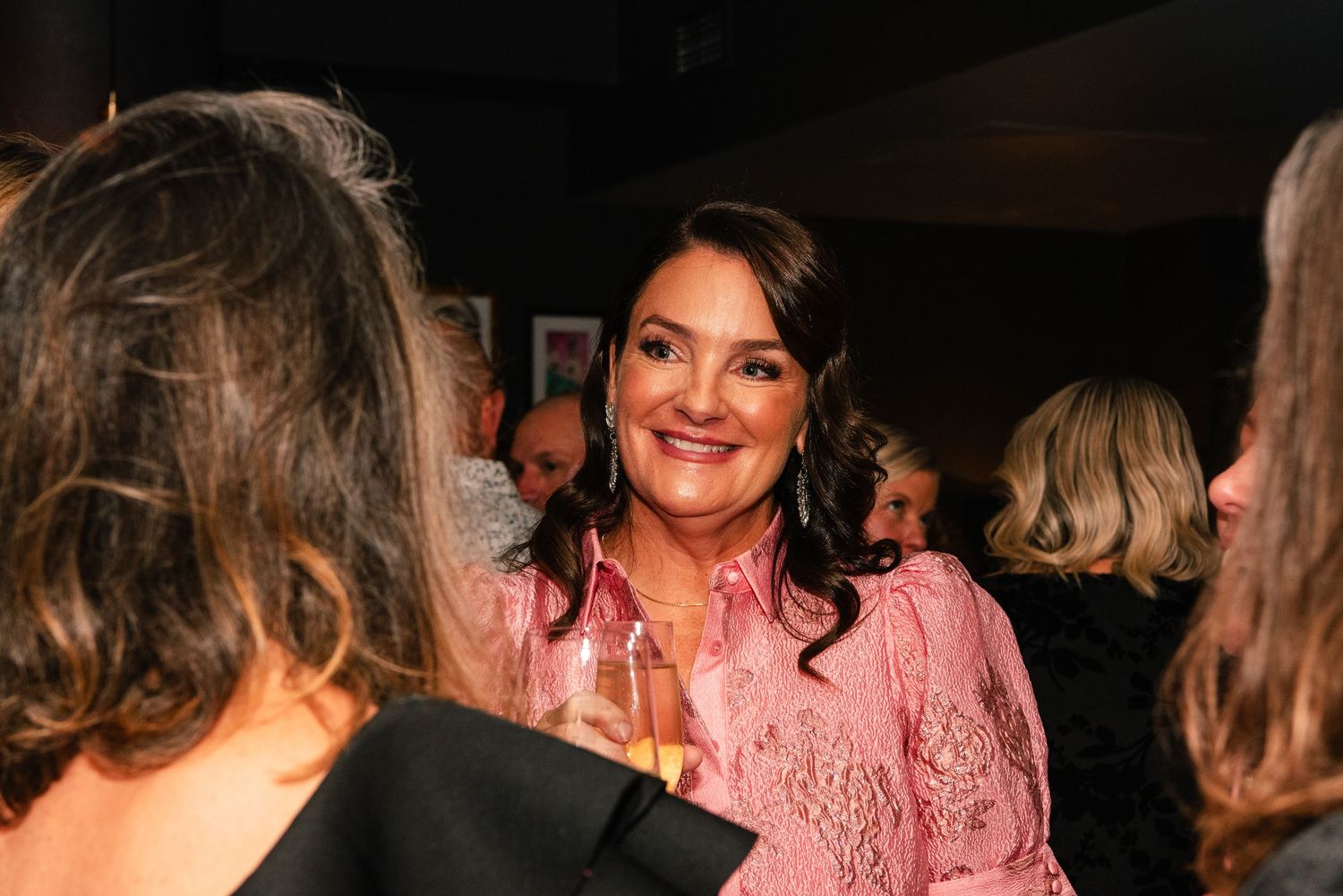 Woman in pink lace top smiling and holding champagne glass at an elegant social gathering event.
