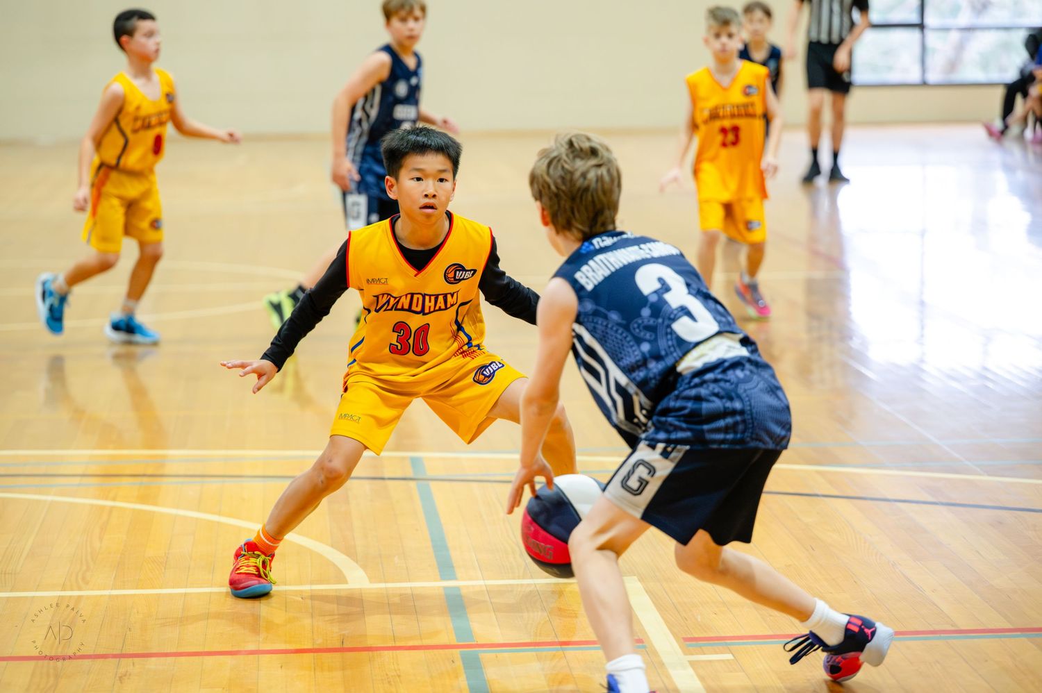 Young boys playing competitive indoor basketball game, with player number 30 in yellow jersey defending against opponent in blue.