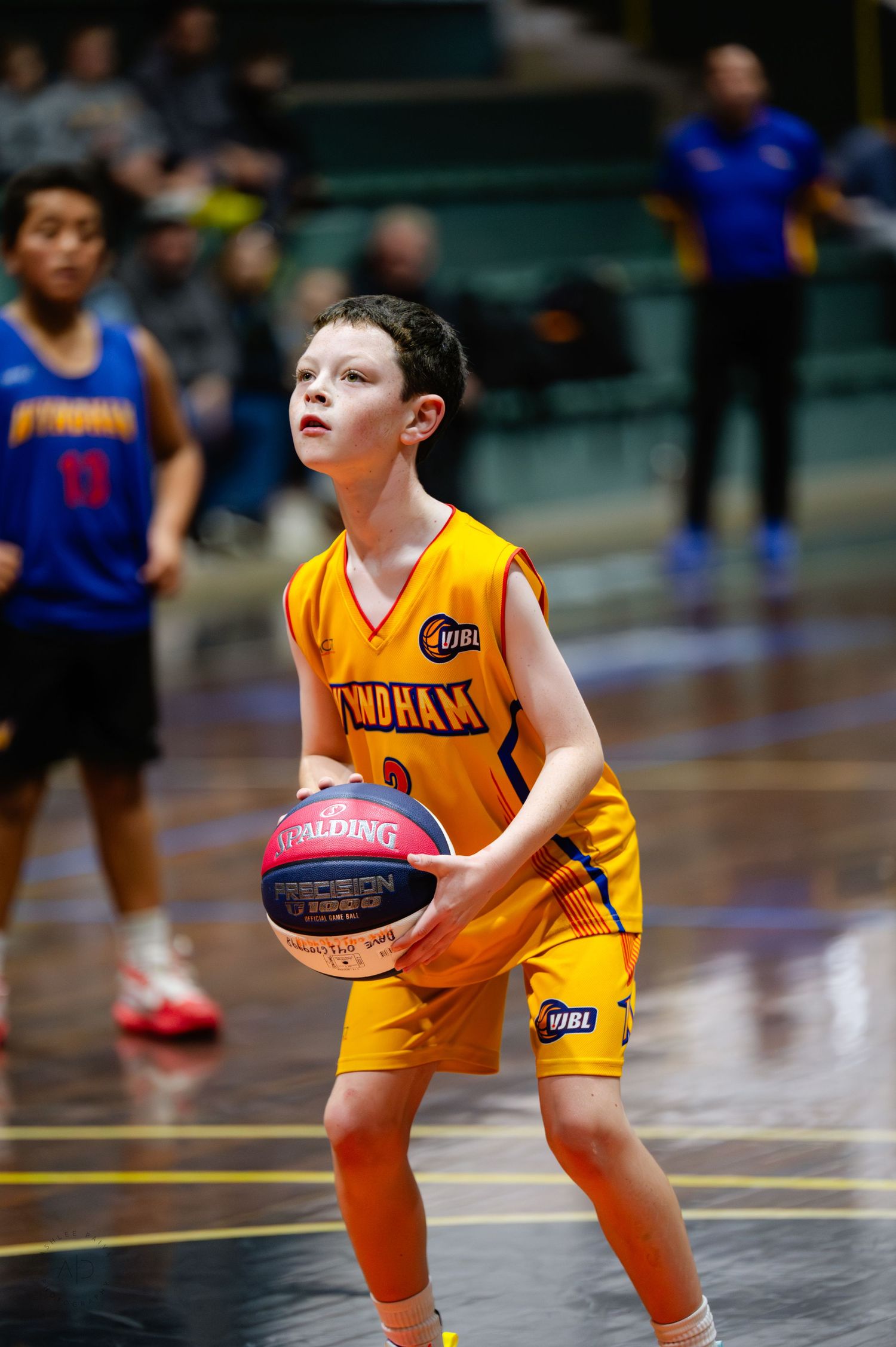 Young boy in yellow Wyndham basketball jersey holds Spalding ball on indoor court during youth league game.