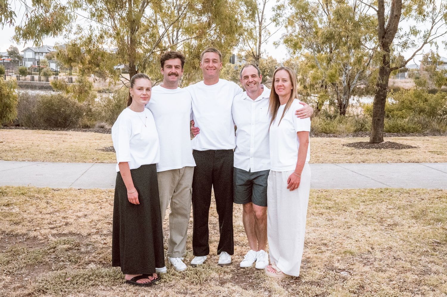 A group in white outfits poses together in a natural outdoor setting with trees.