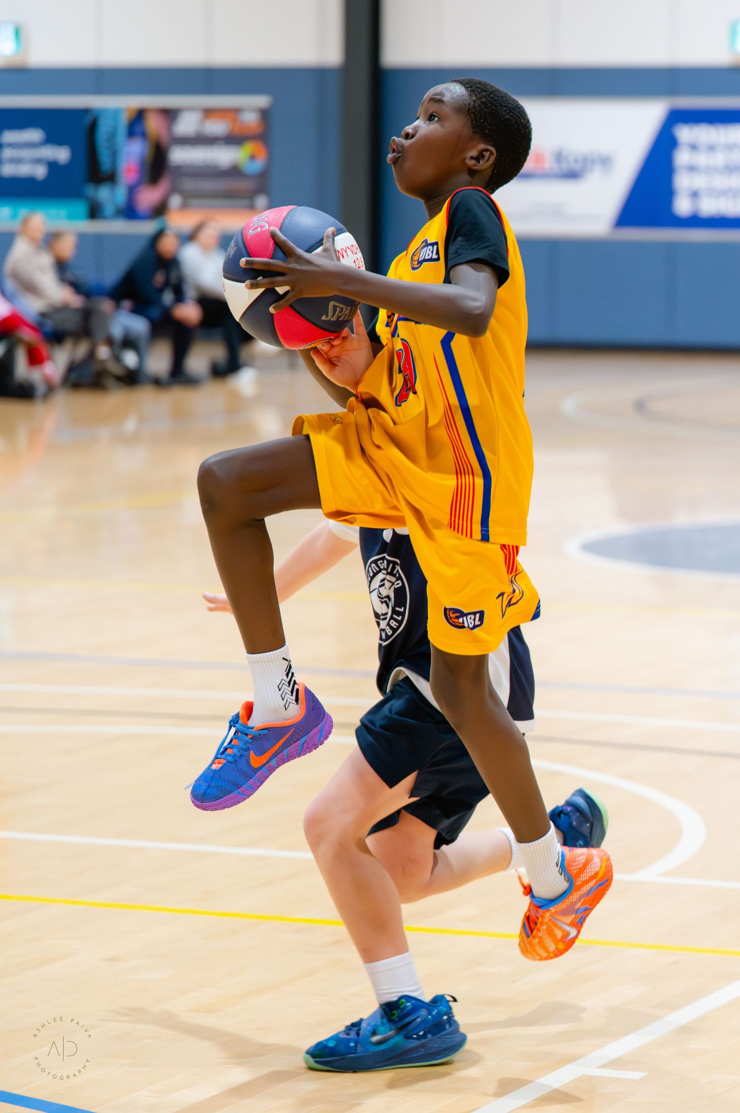 Two youth basketball players in yellow uniforms compete for the ball during an indoor game.