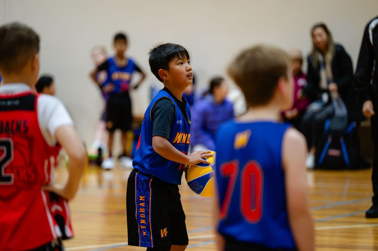 Young boy in blue basketball uniform holds ball during indoor youth basketball game.