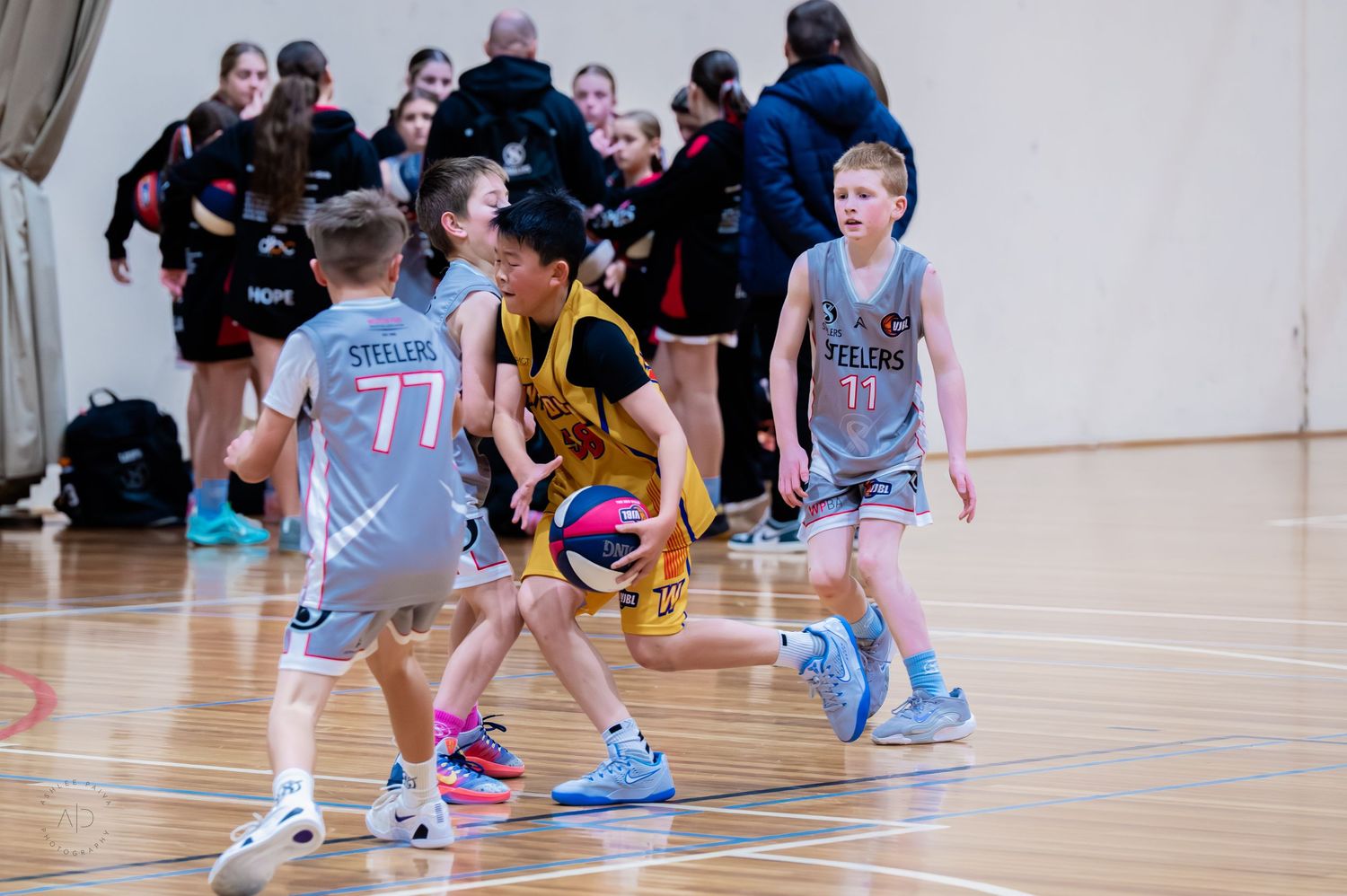 Young basketball players compete in an indoor youth game, with players in gray and yellow uniforms dribbling on court.