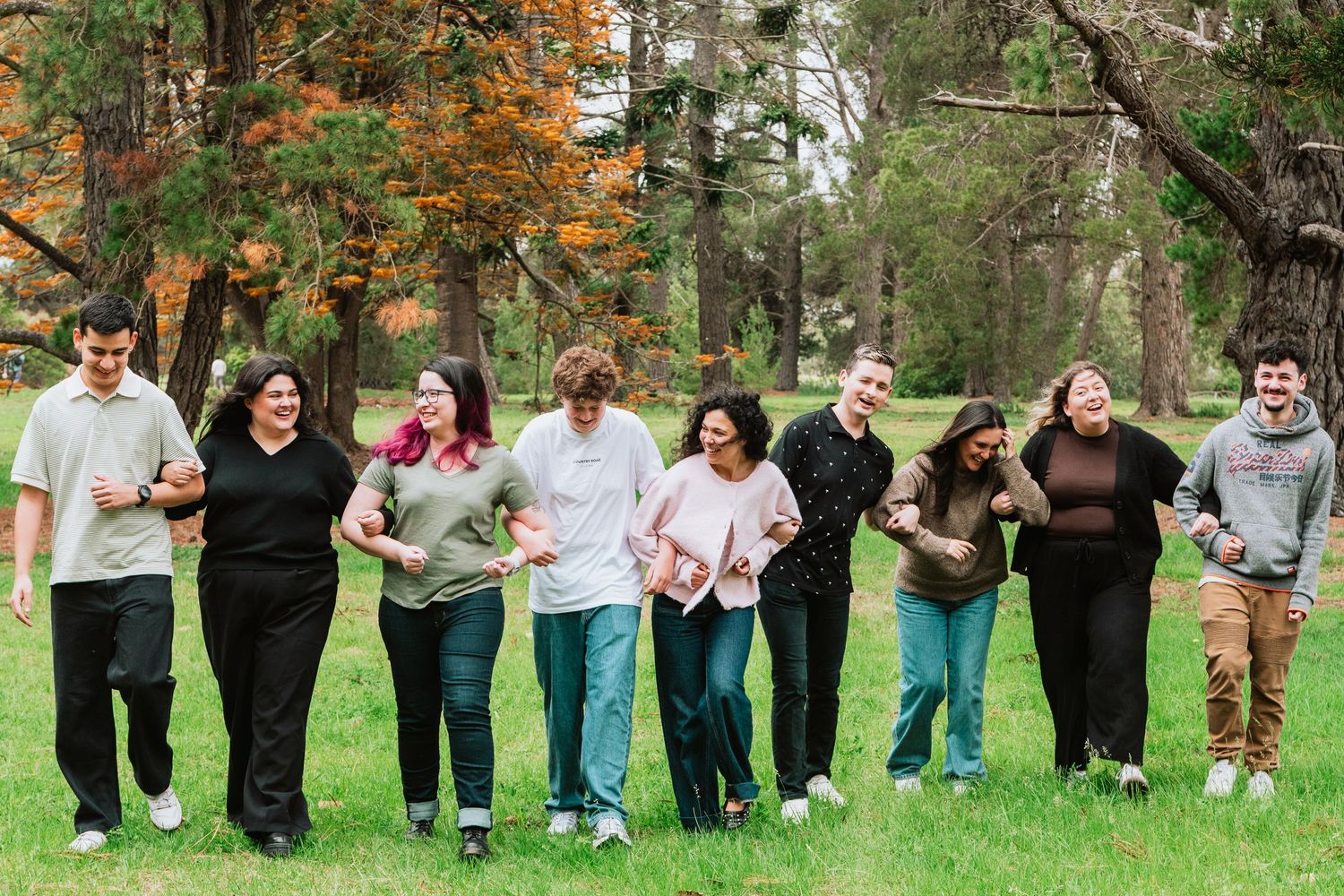 Large group of people lined up outdoors against a backdrop of autumn trees and grass.