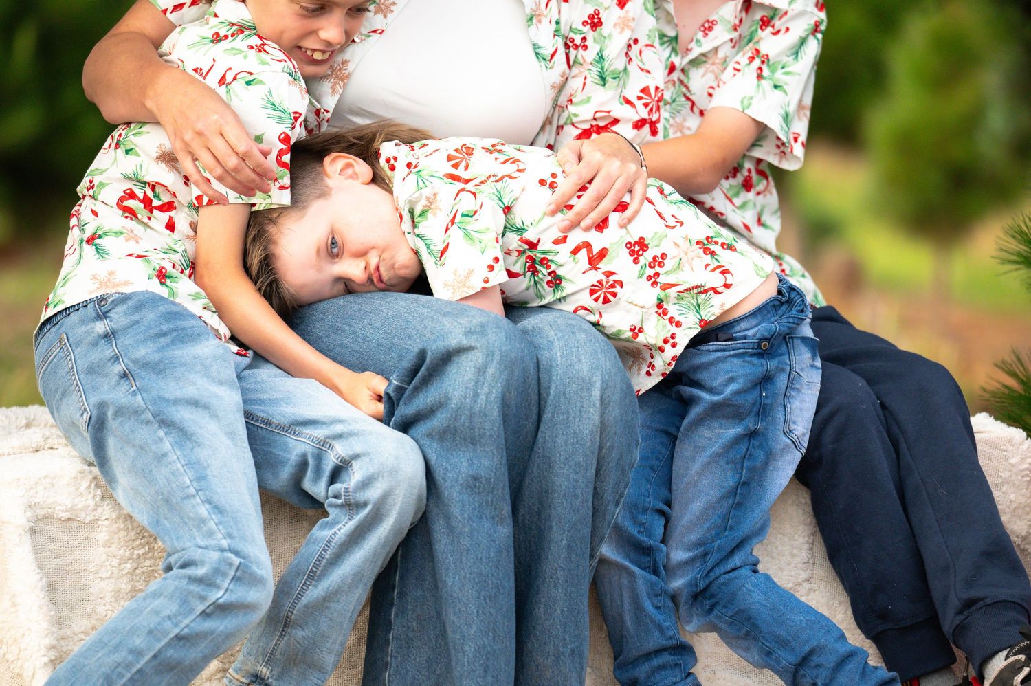 Family members sitting close together on rustic steps with pine trees in background.