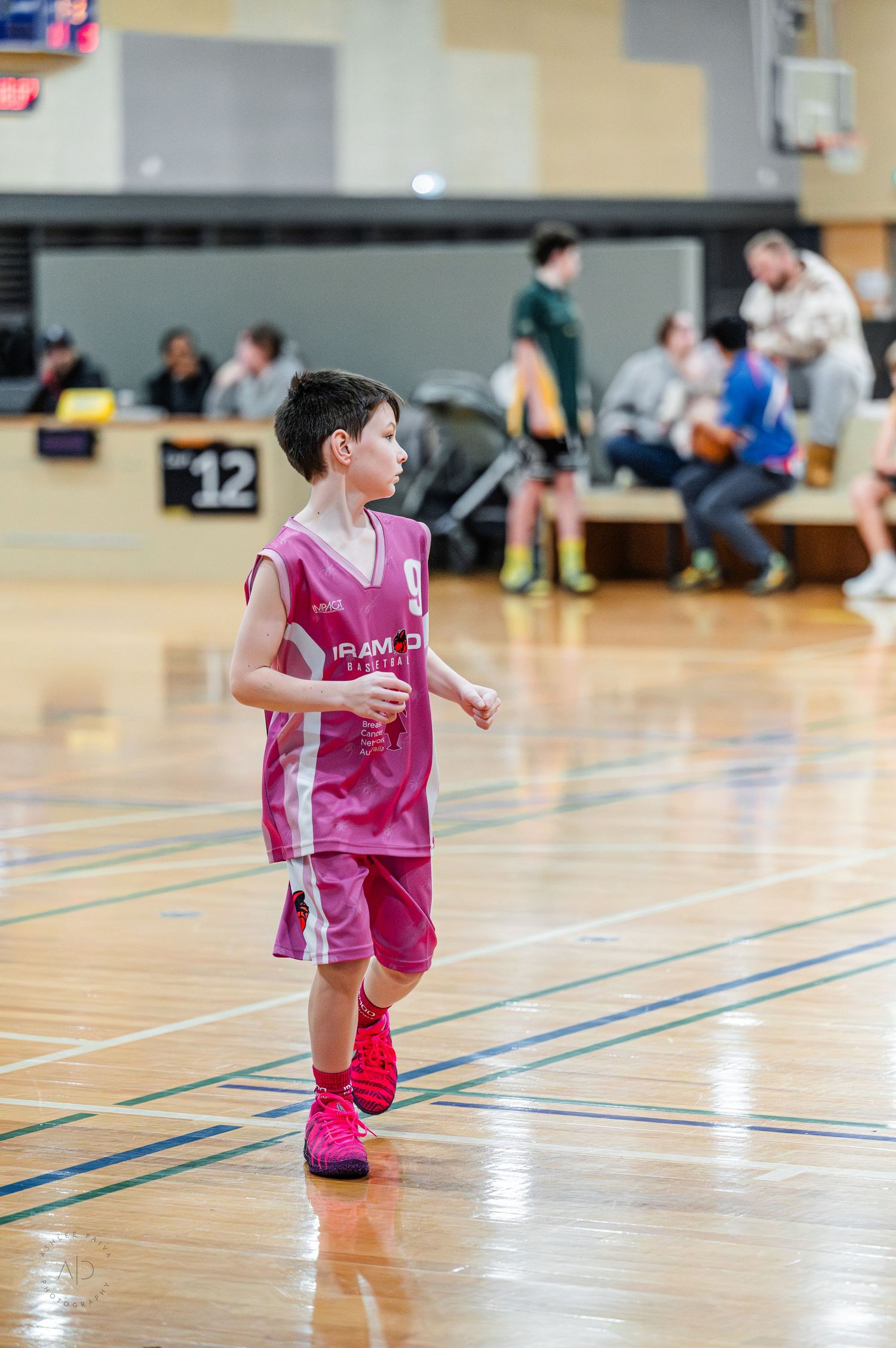 Young boy in pink basketball uniform dribbling on indoor court during youth basketball game.