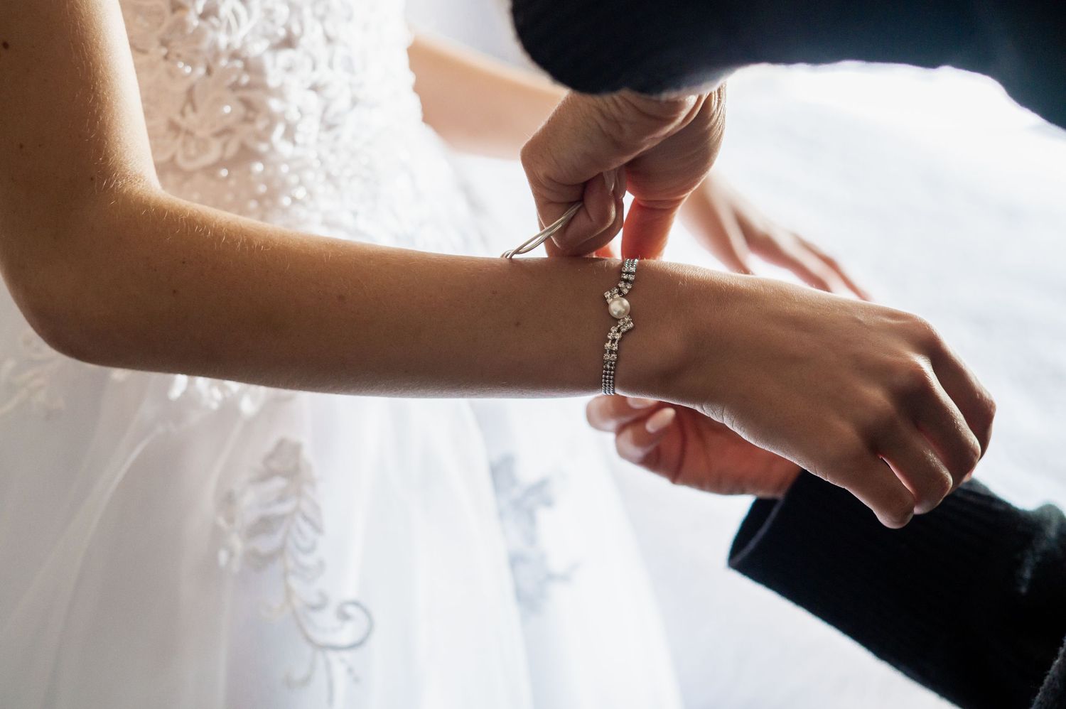 Groom fastening a delicate diamond bracelet on bride's wrist during wedding day preparations.