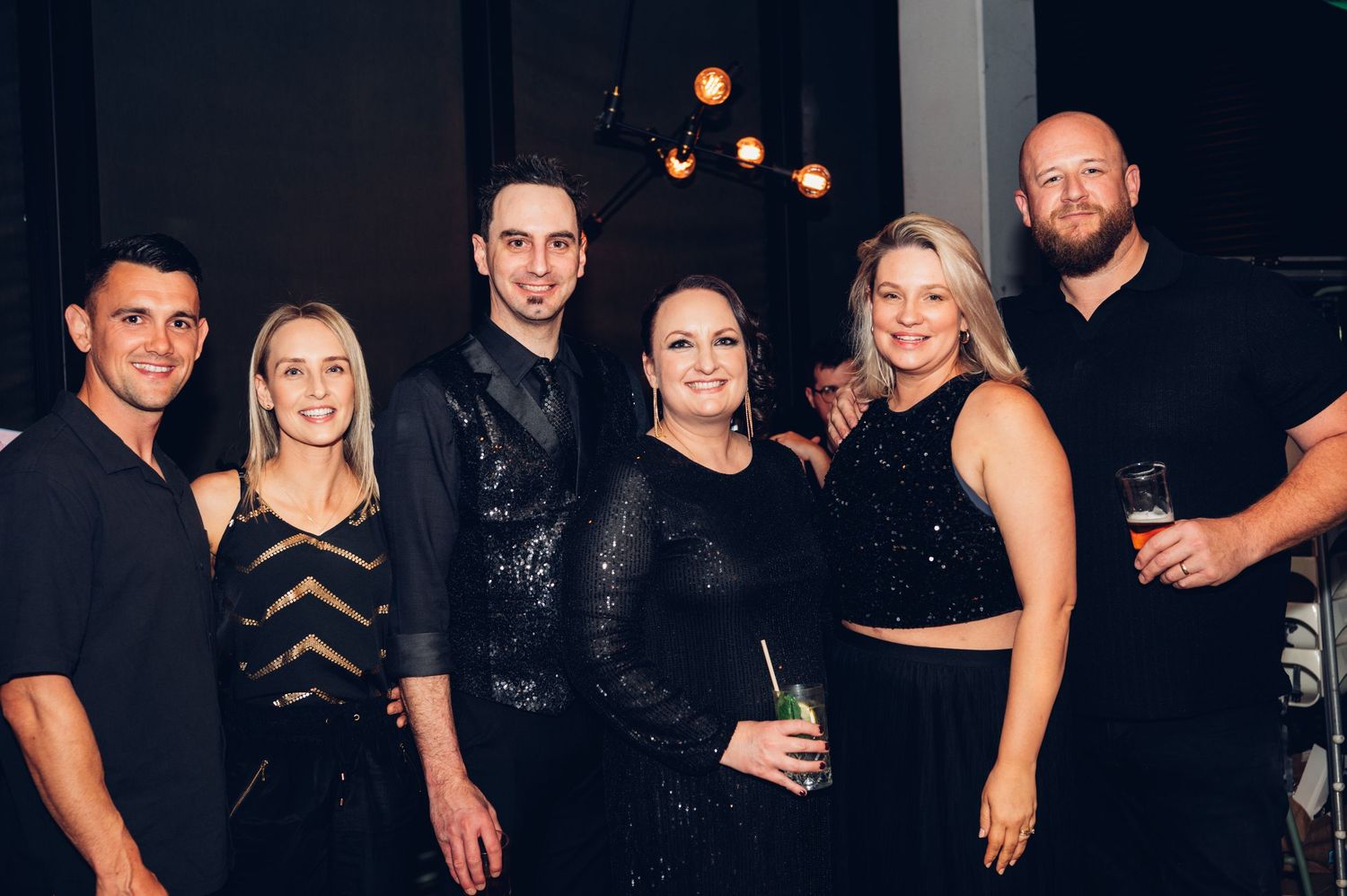 A group of friends dressed in formal black attire pose together at an evening event.