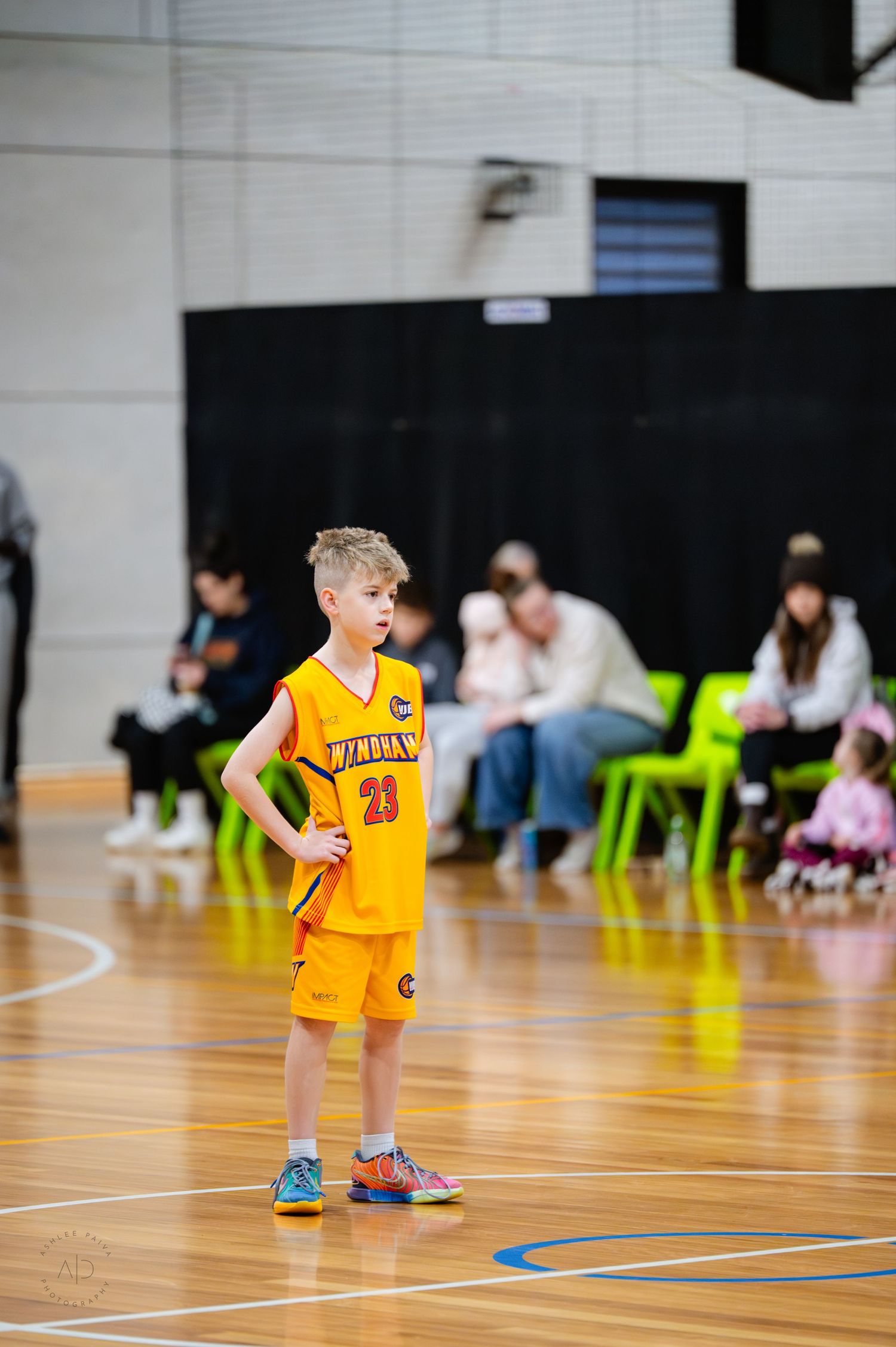 Young boy in yellow basketball uniform standing on indoor court during a youth basketball game.