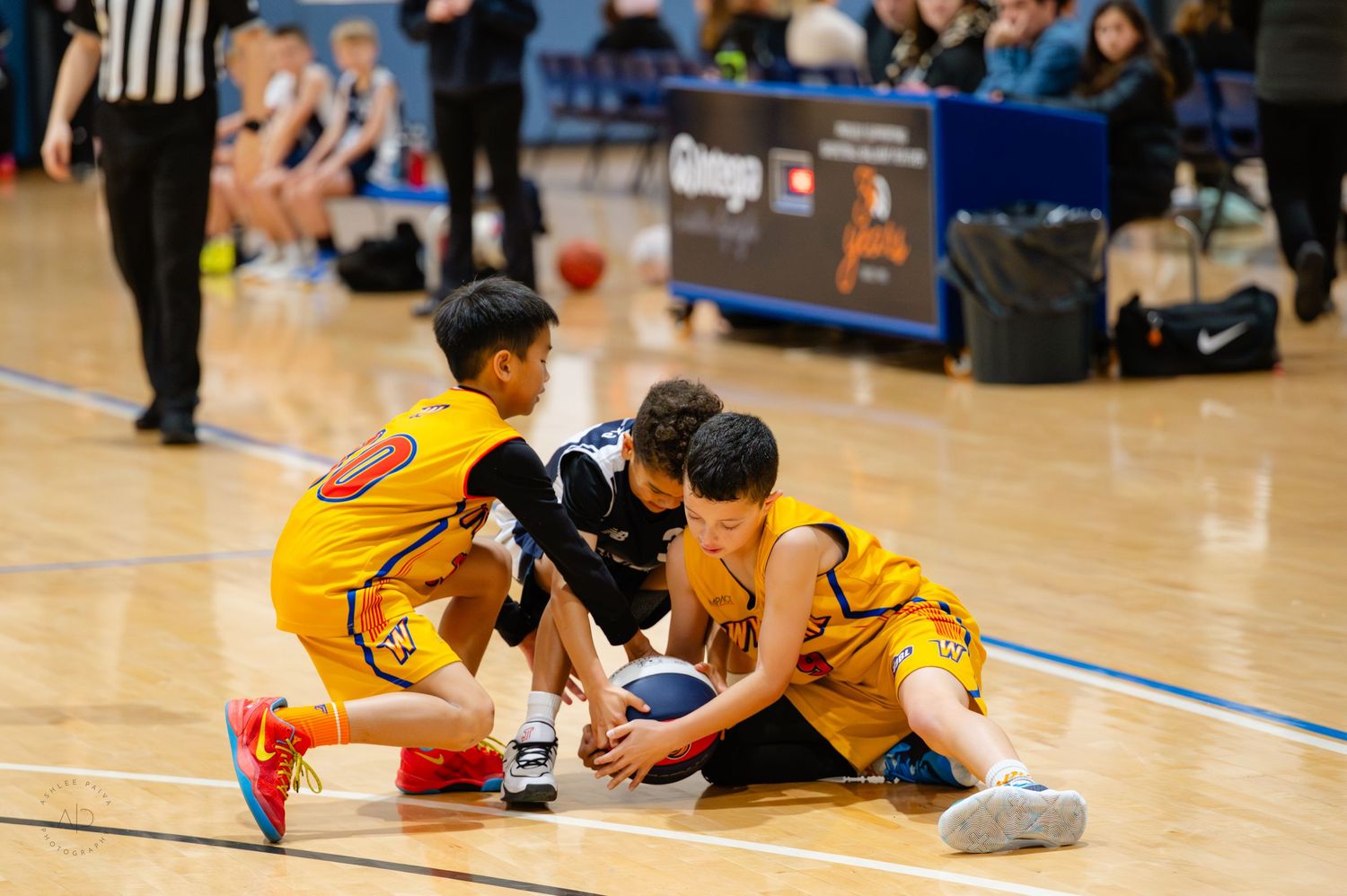 Young basketball players scramble for a loose ball on an indoor court during a youth basketball game.