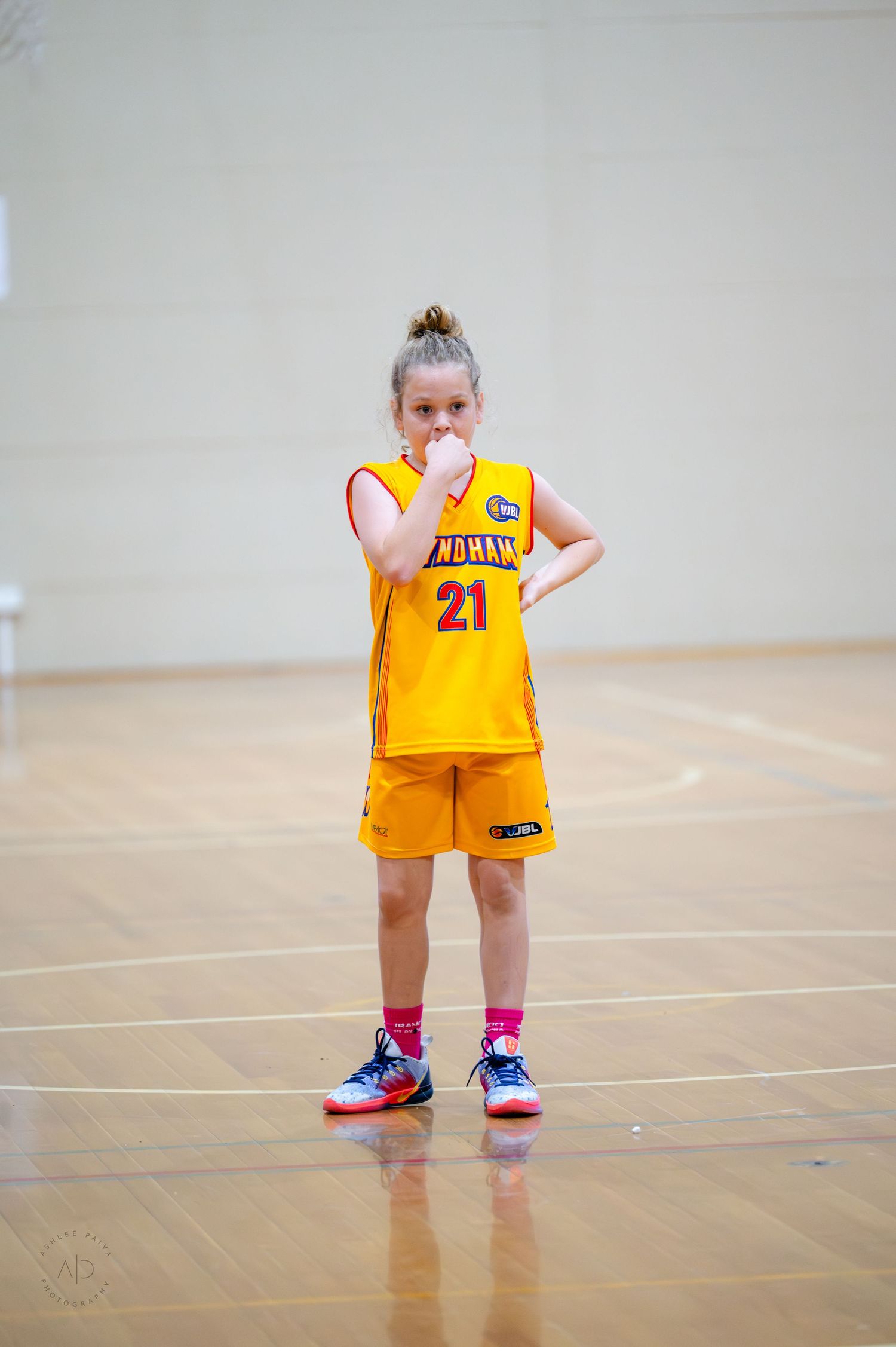 Young girl in yellow basketball uniform number 21 standing on indoor court during a youth basketball game.