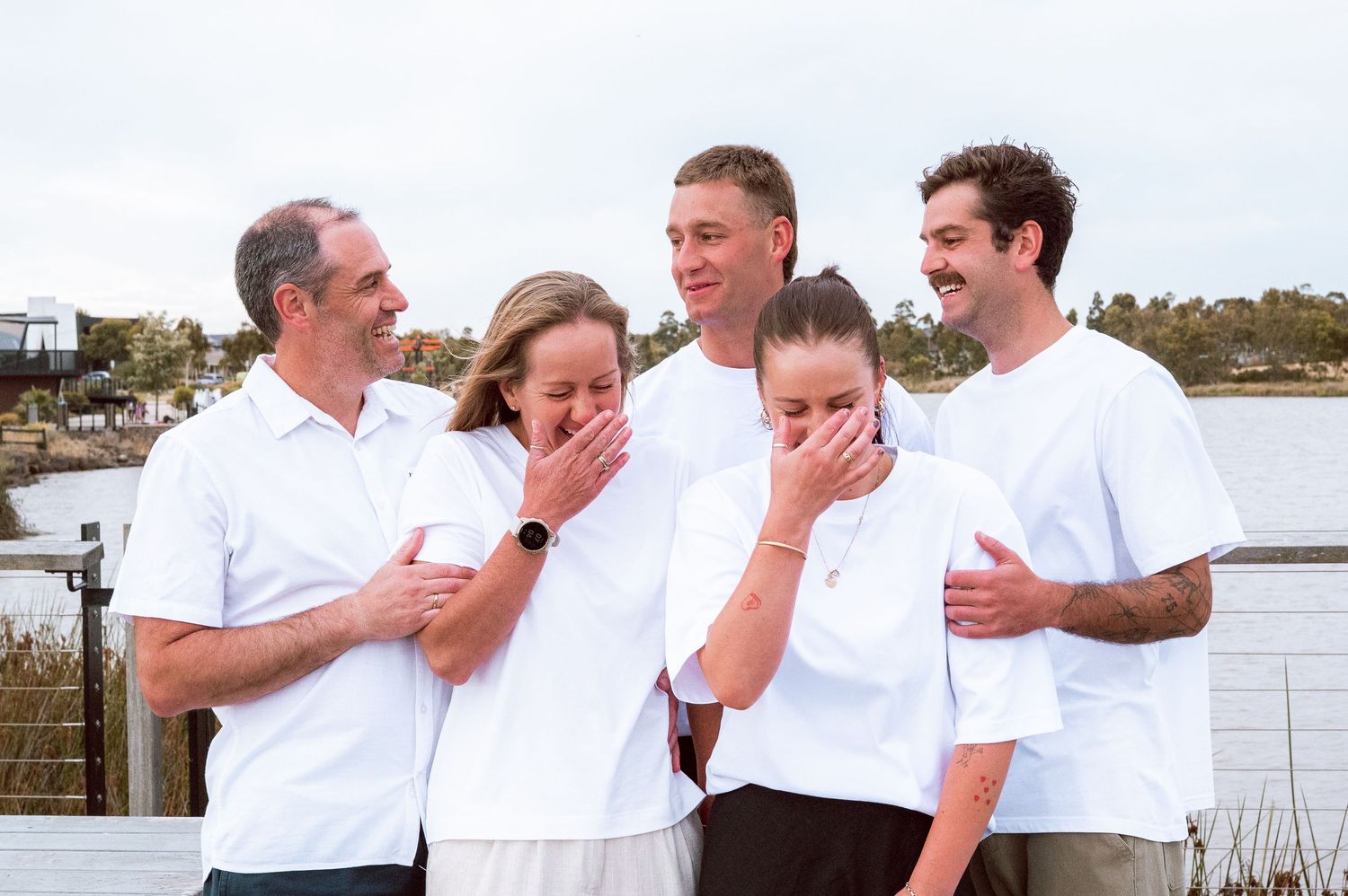 A group in white shirts shares a candid laughing moment by the waterfront.