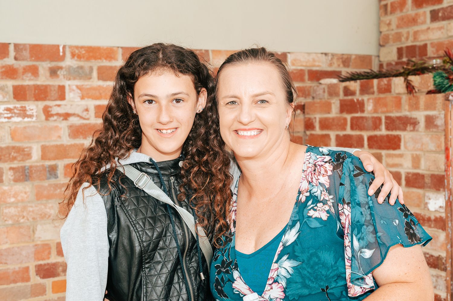 Two people wearing blue and black outfits pose together in front of a brick wall background.