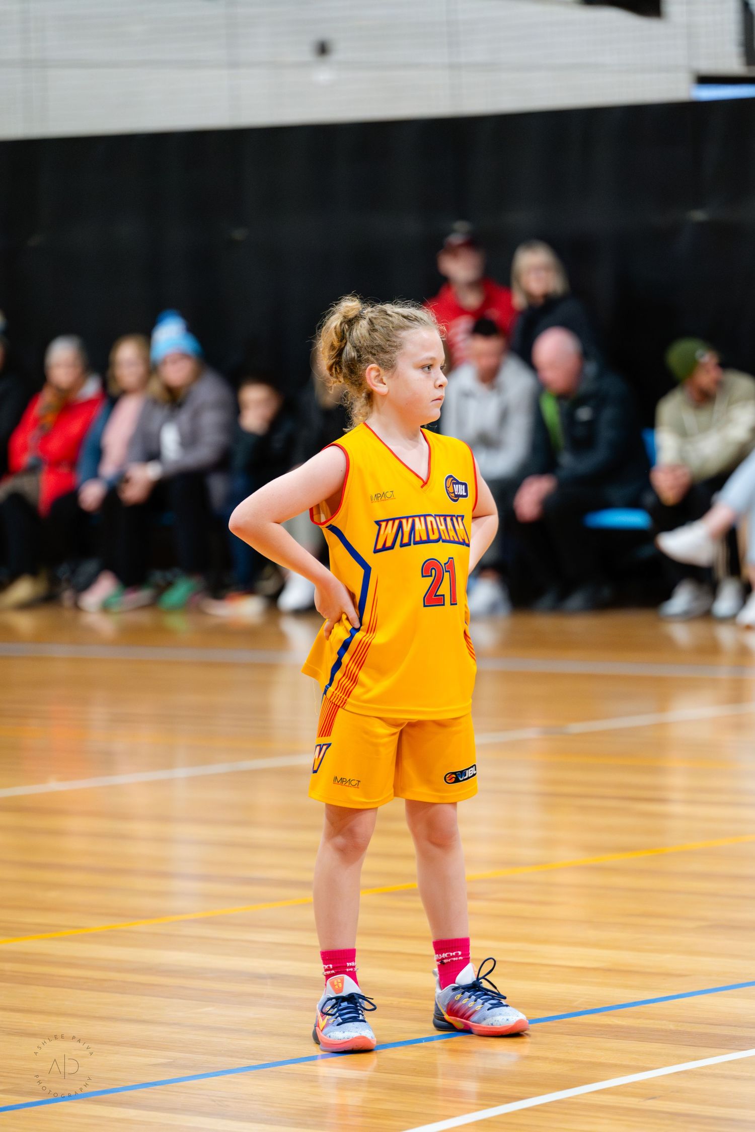 Young girl in yellow Wyndham #21 basketball uniform stands on court during a junior basketball game.