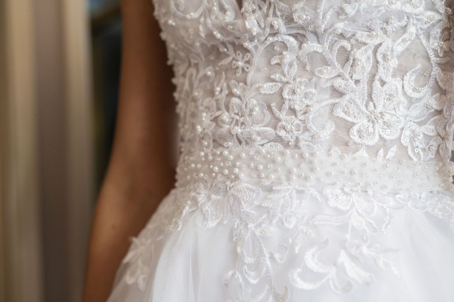 Close-up of a bridal gown bodice featuring intricate lace floral embroidery with pearl beading details.
