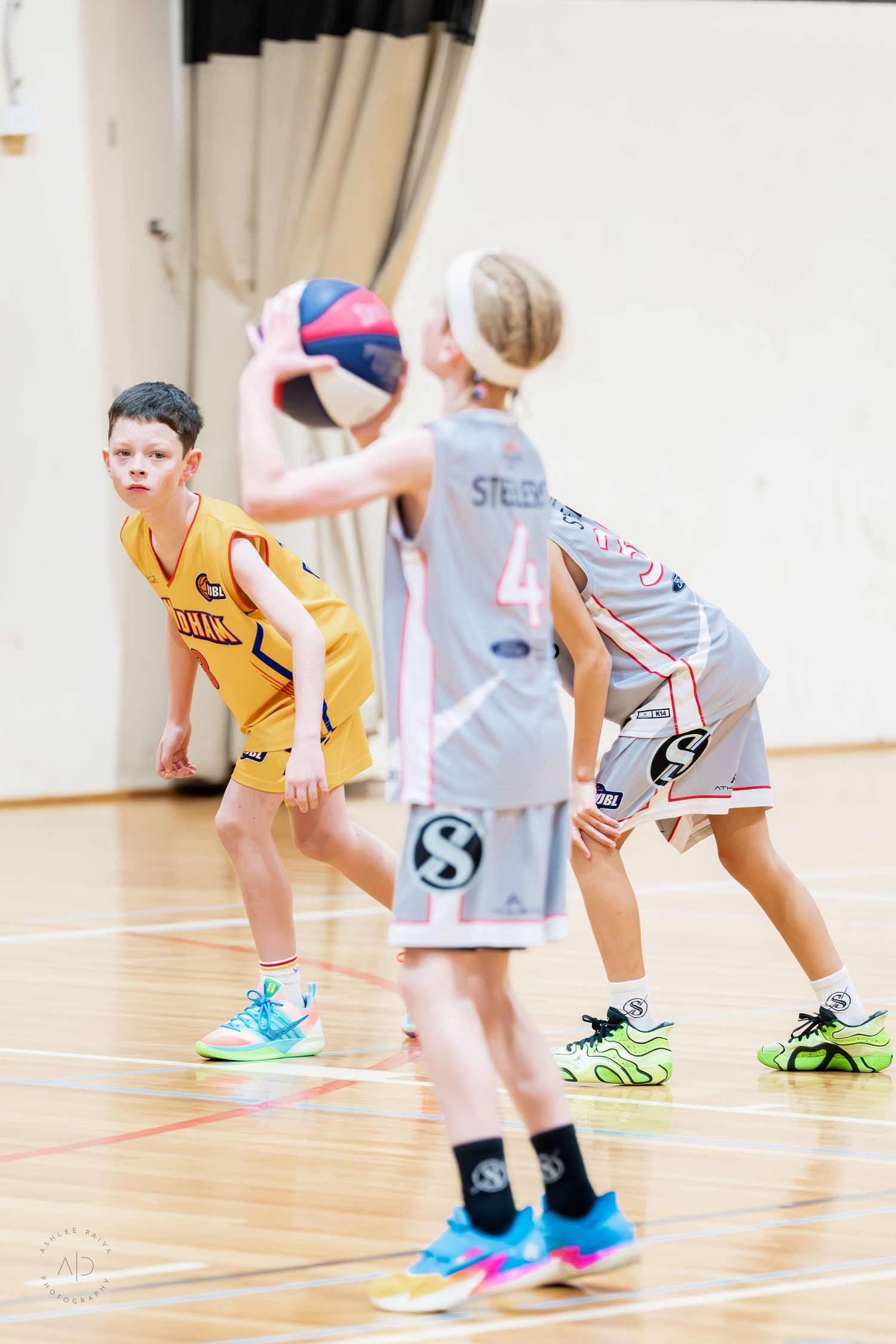 Young boys playing basketball in a gym, one holding the ball while defenders guard in colorful sneakers.